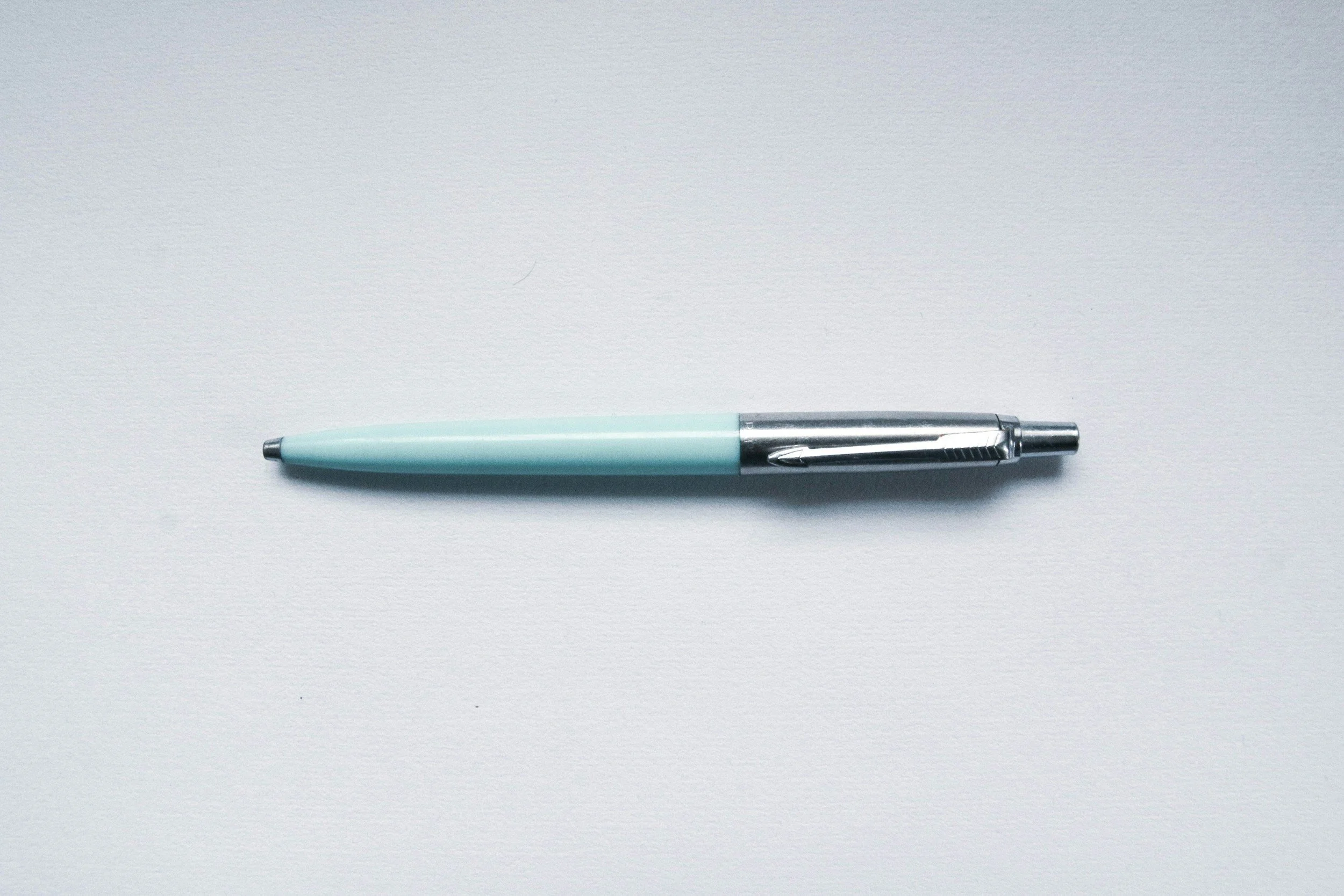 A light blue pen with silver accents lying horizontally on a white surface.
