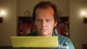 A man with medium-length hair looking down at a yellow typewriter in front of him.