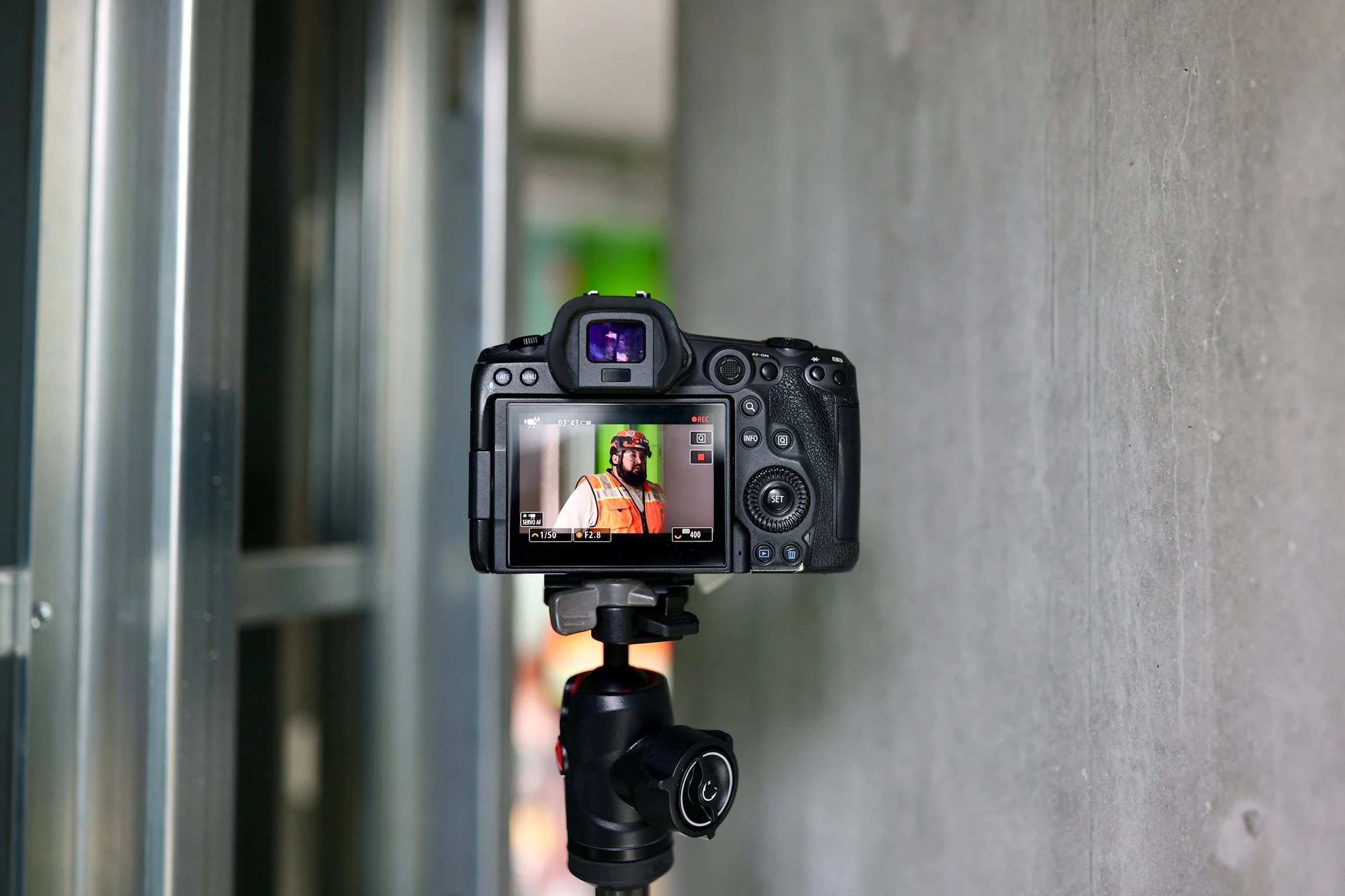 A professional camera mounted on a tripod, capturing a worker in safety gear on a construction site.