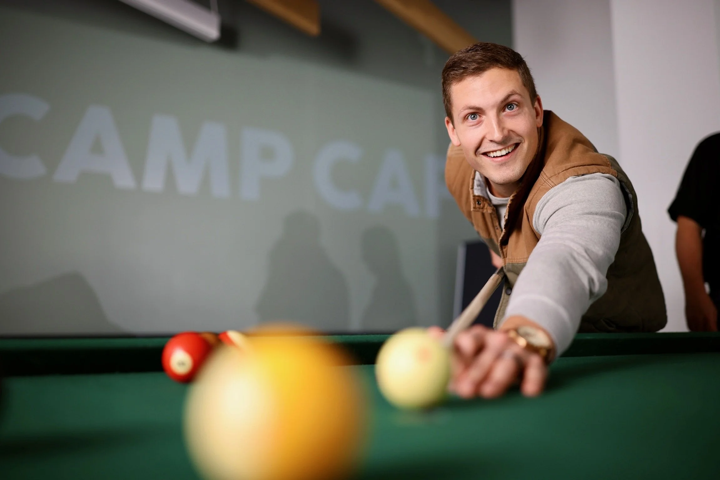 A young man playing pool or billiards, smiling, leaning over the pool table.