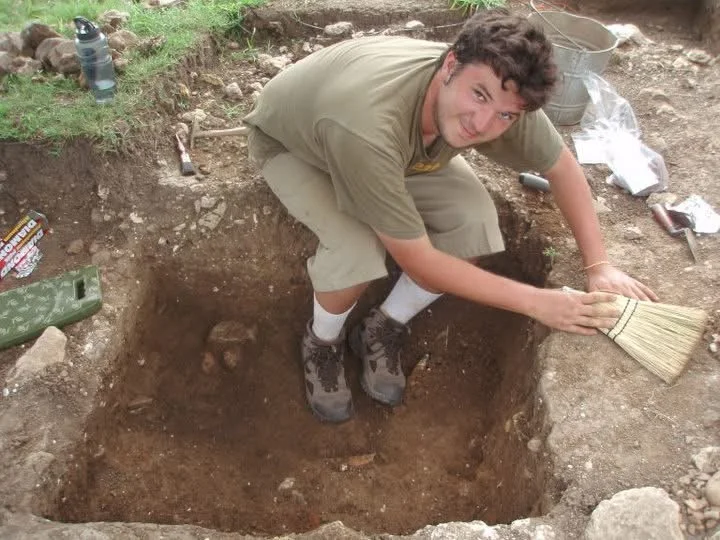 A young Thomas Wingate, democratic central committee candidate for district 46, poses in an excavation unit, some artifacts are visible in the dirt
