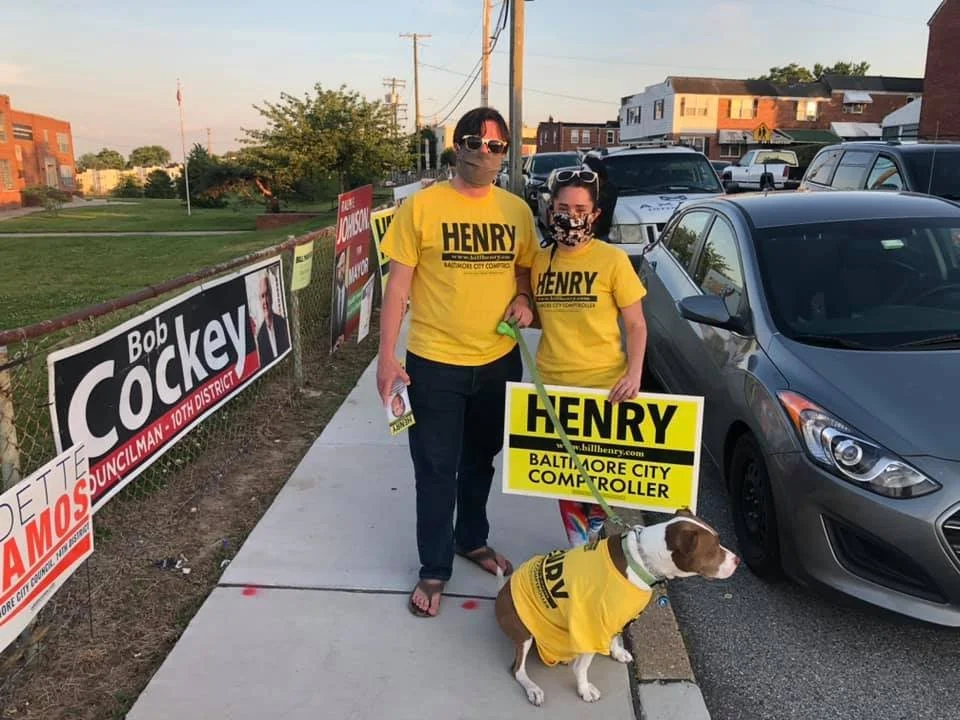 Baltimore City democratic central committee Candidate Thomas Wingate and his wife in matching "Bill Henry for Comptroller" shirts outside a polling location. They holding a sign and wearing covid masks