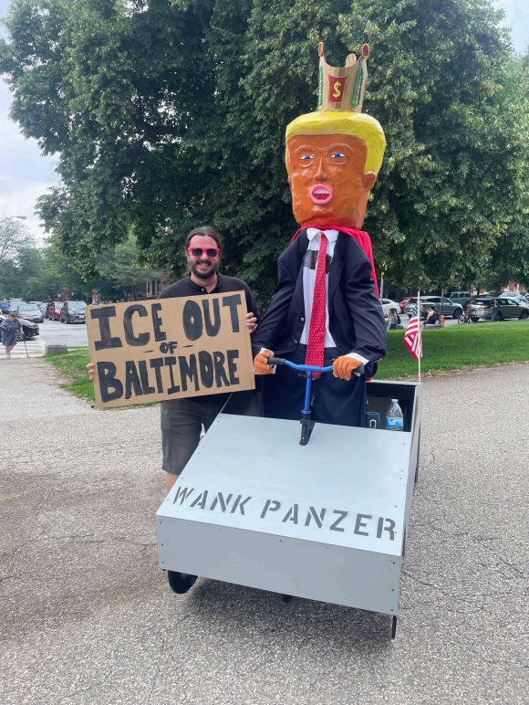 District 46 candidate Thomas Wingate is next to an art piece mocking Donald Trump, he is holding a sign that says "ICE Out of Baltimore"