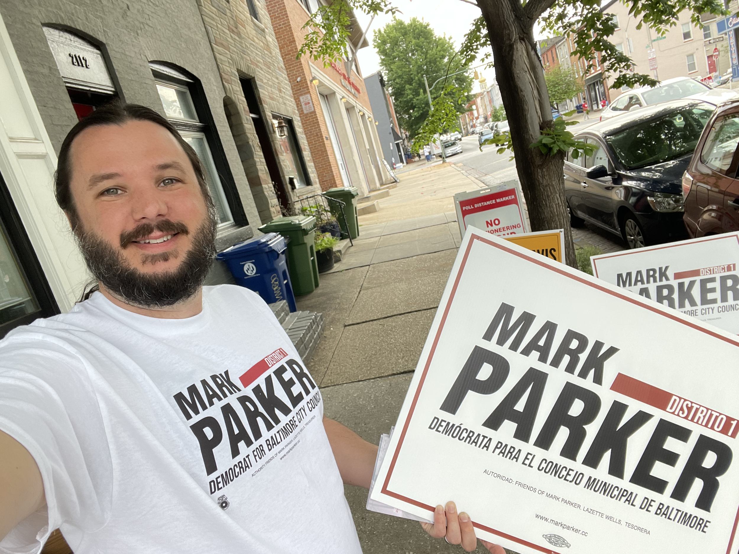 District 46 Candidate Thomas Wingate is wearing a "Mark Parker, Democrat for Baltimore City Council" shirt and holding a similar sign on a street in Baltimore