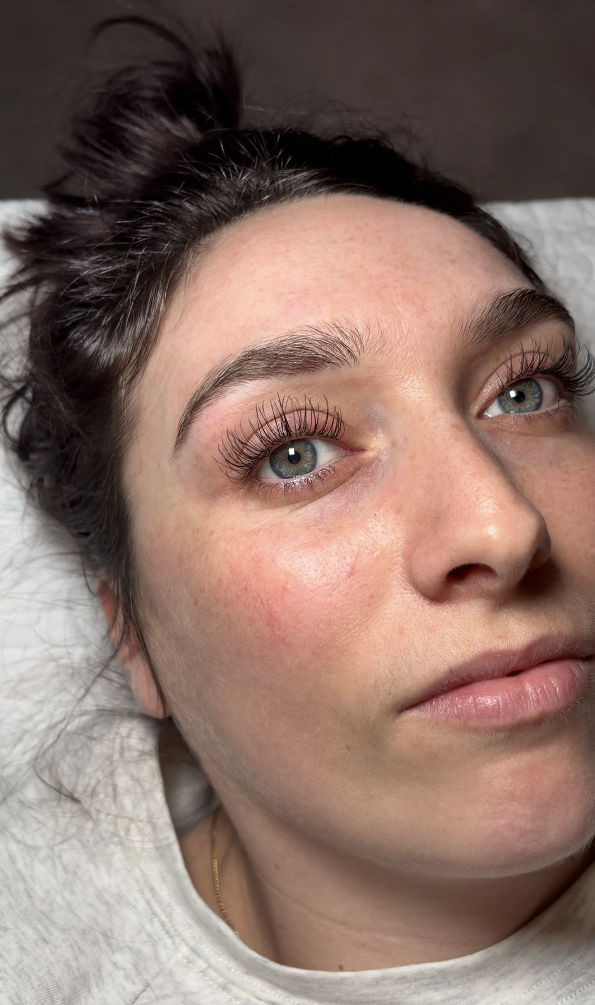 Close-up of a woman with blue eyes, natural makeup, and long curled eyelashes lying down on a pillow.
