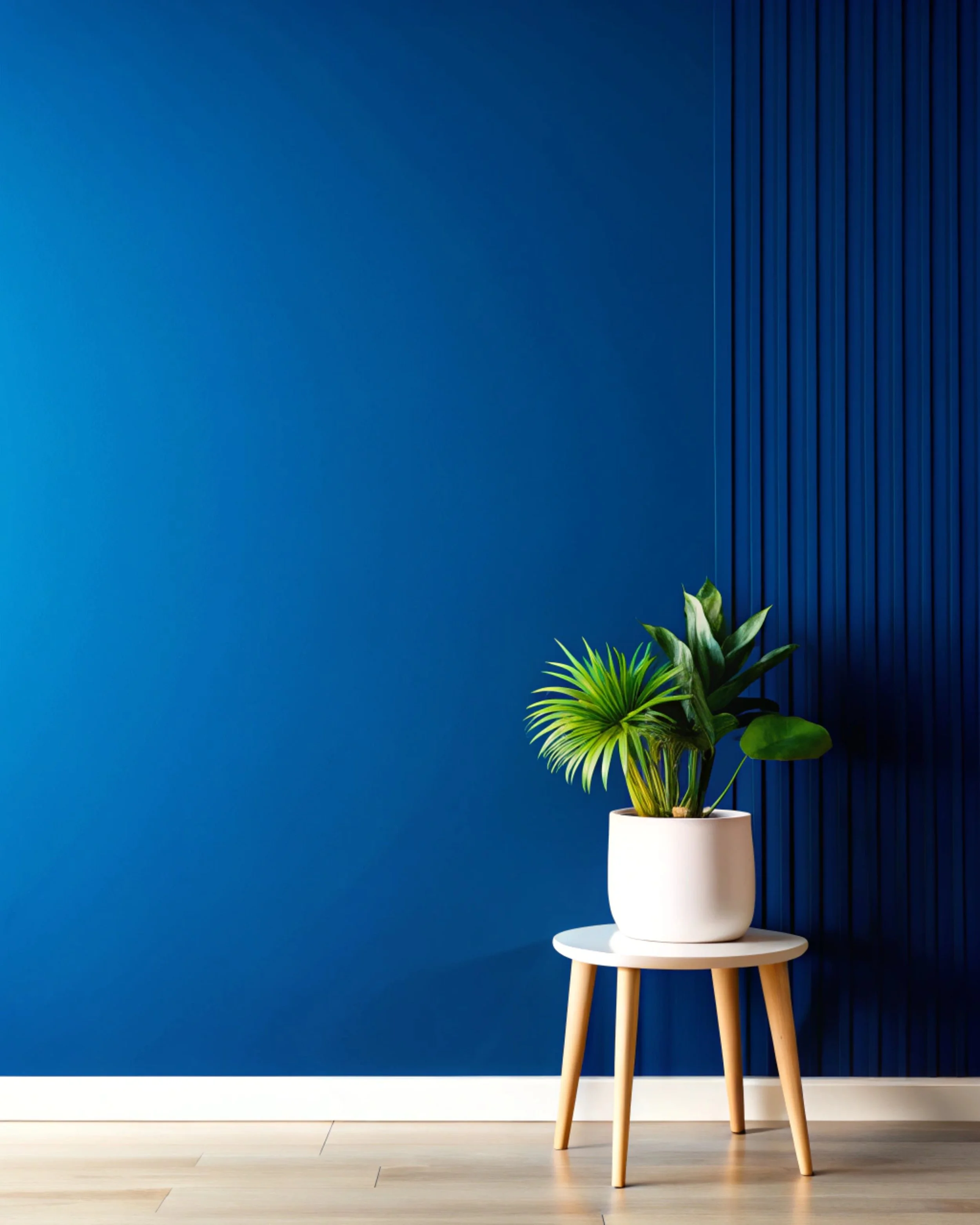 Green houseplant in white pot on small wooden table in front of a blue wall with textured paneling.