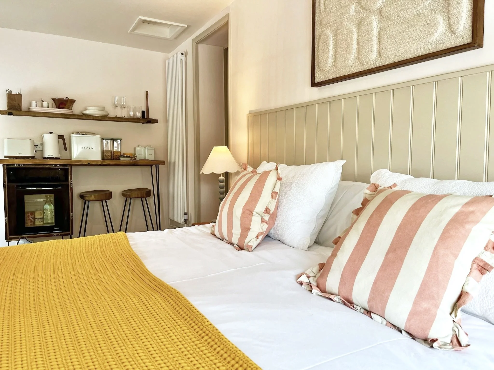 Close-up view of a bed with white and pink striped pillows, a white blanket, a yellow textured blanket, and a wooden headboard in a cozy bedroom.