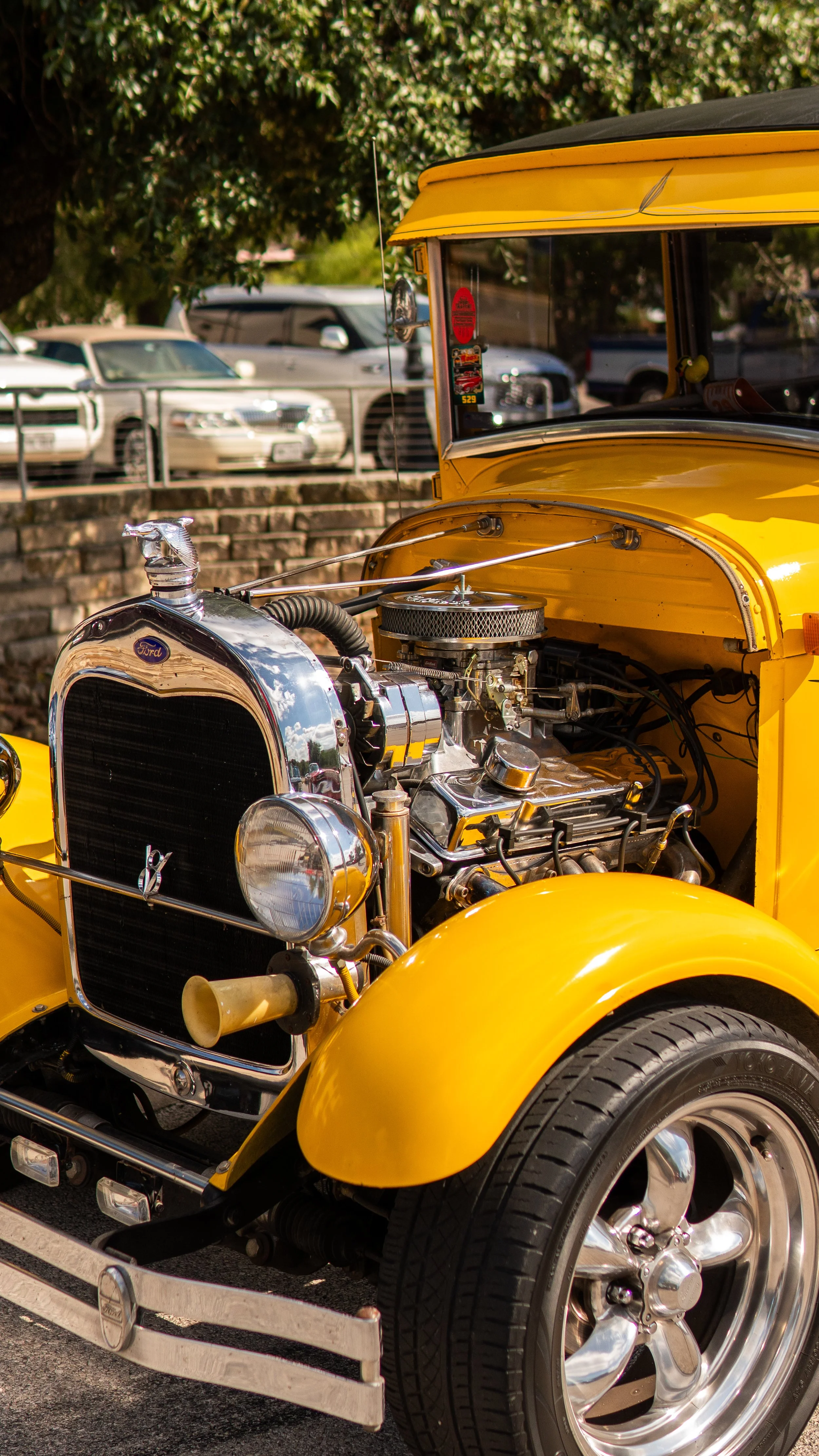Vehículo clásico amarillo con motor expuesto y logotipo de Ford en la parrilla.