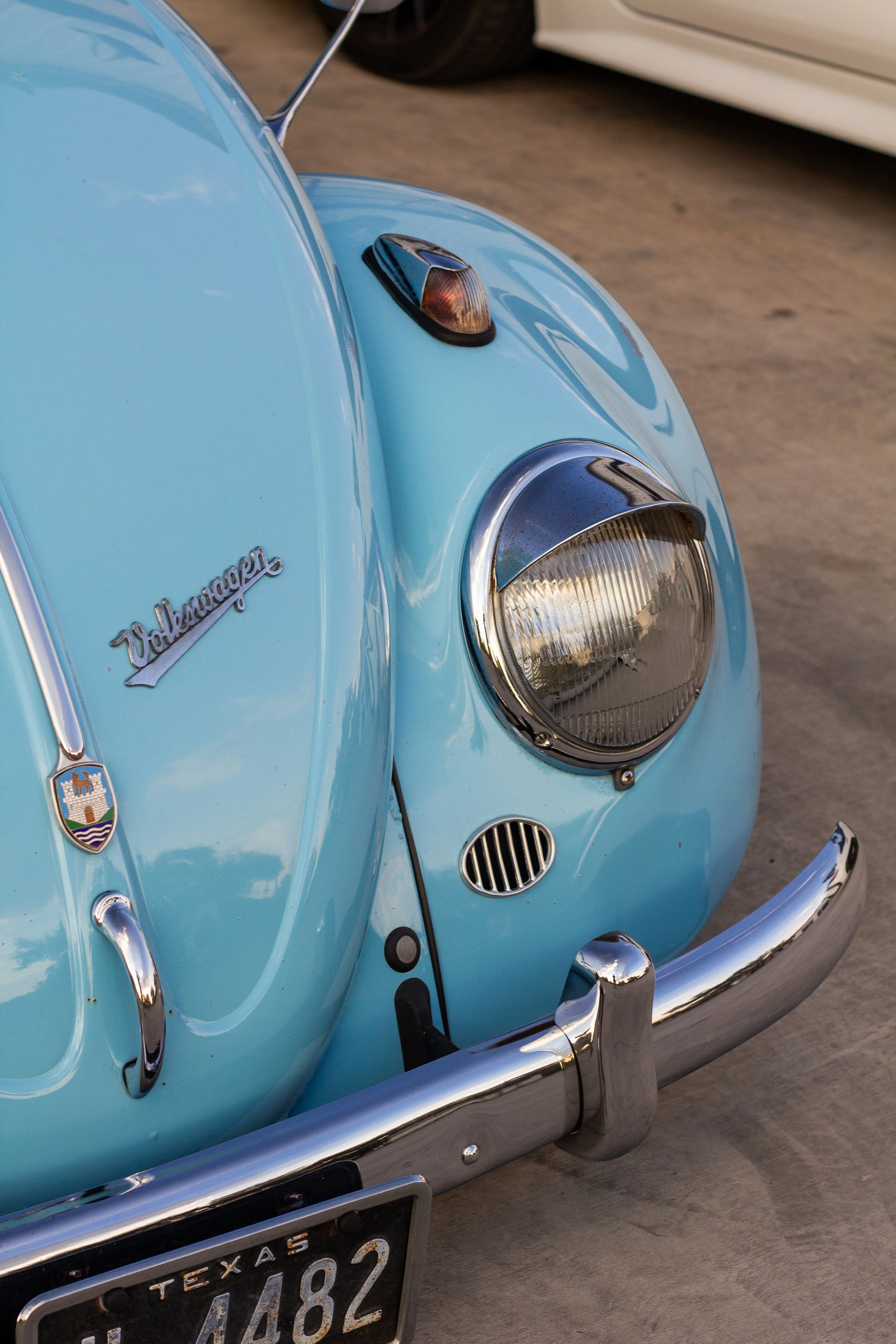 Vista frontal de un coche clásico color azul claro, modelo Volkswagen escarabajo, con detalles cromados y una matrícula de Texas.