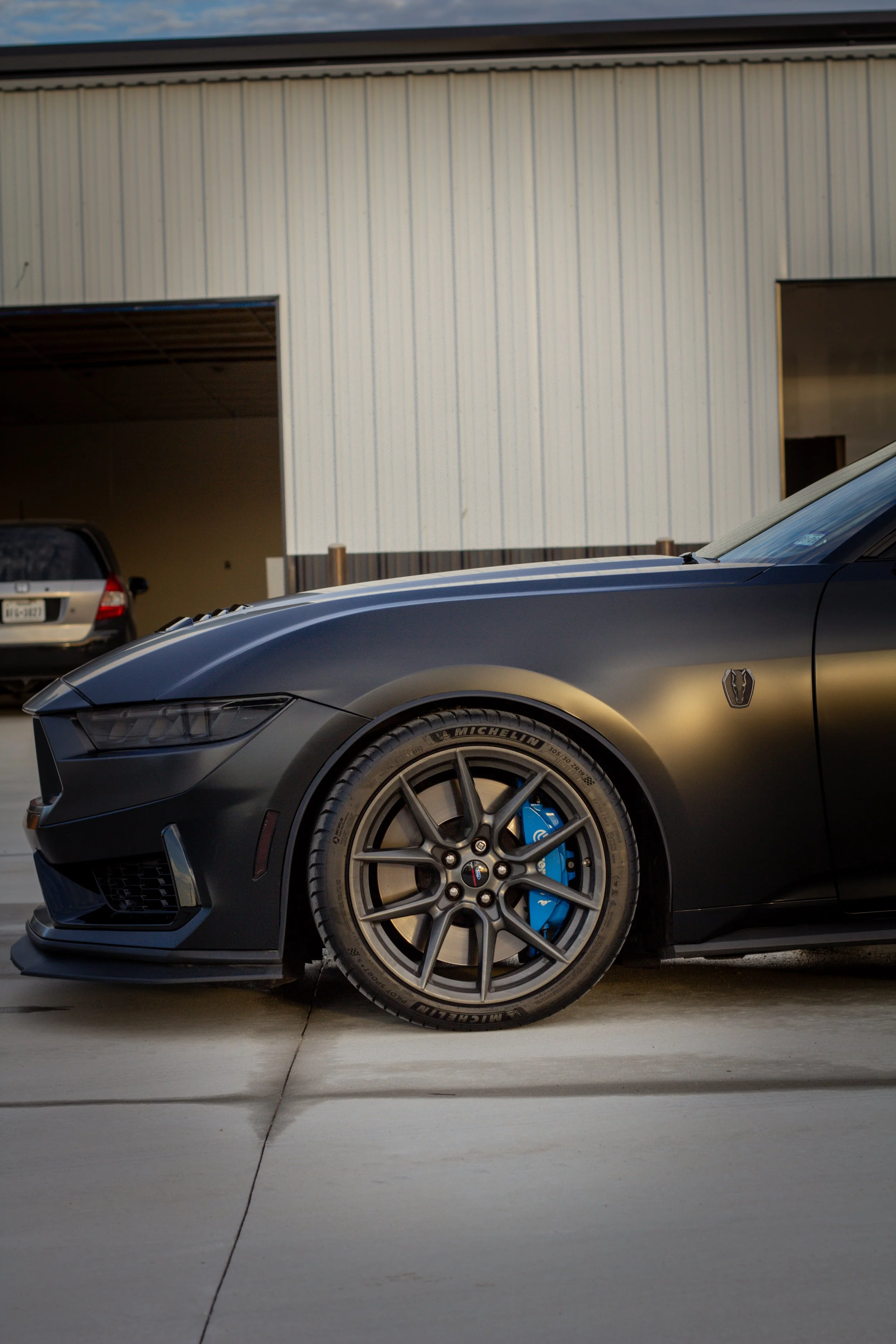 Autos deportivos negros estacionados en un garaje o área de almacenamiento con fondo de pared de metal blanco.