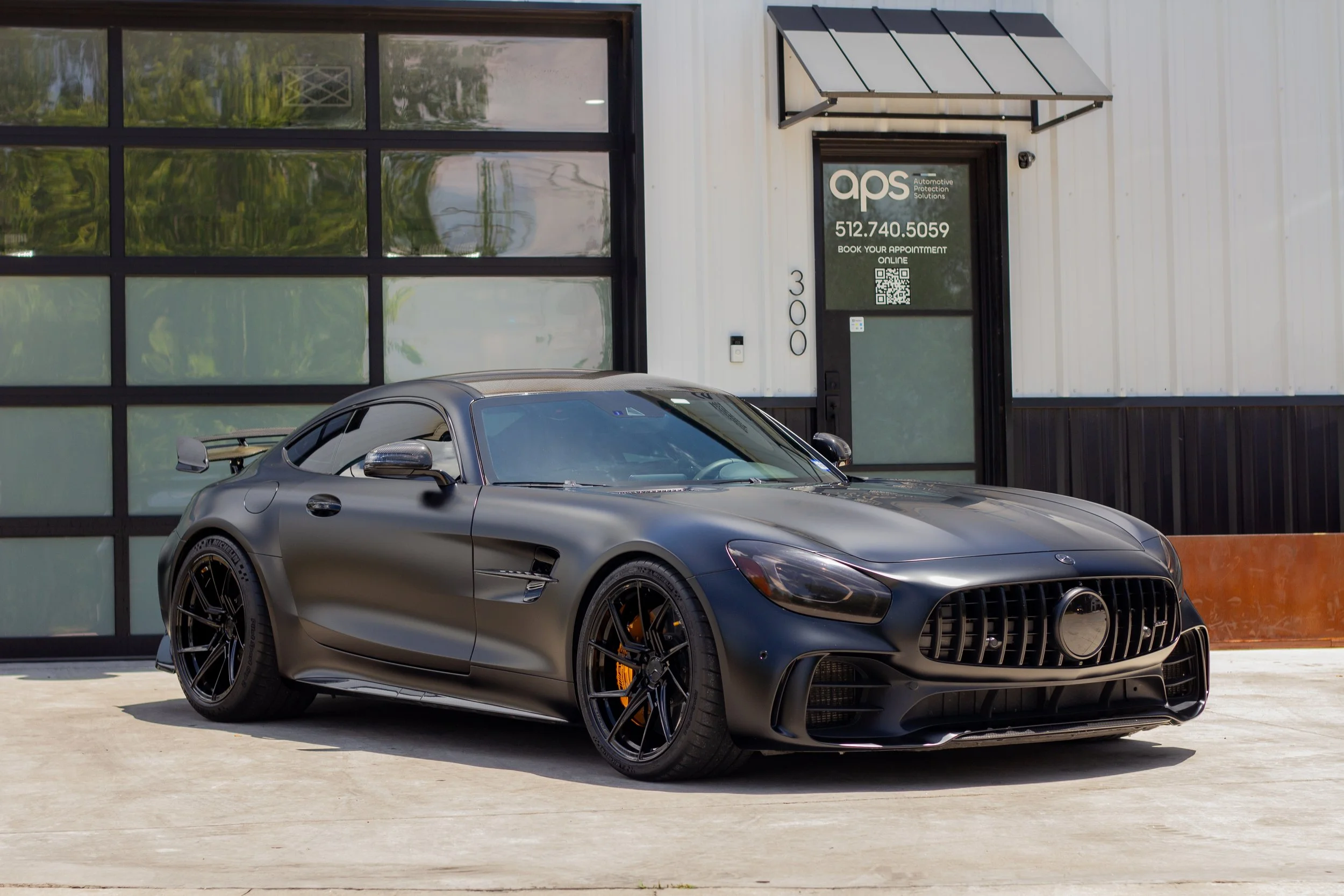 Autos deportivos negros estacionados frente a un edificio con ventanas y puerta de entrada con información de contacto.