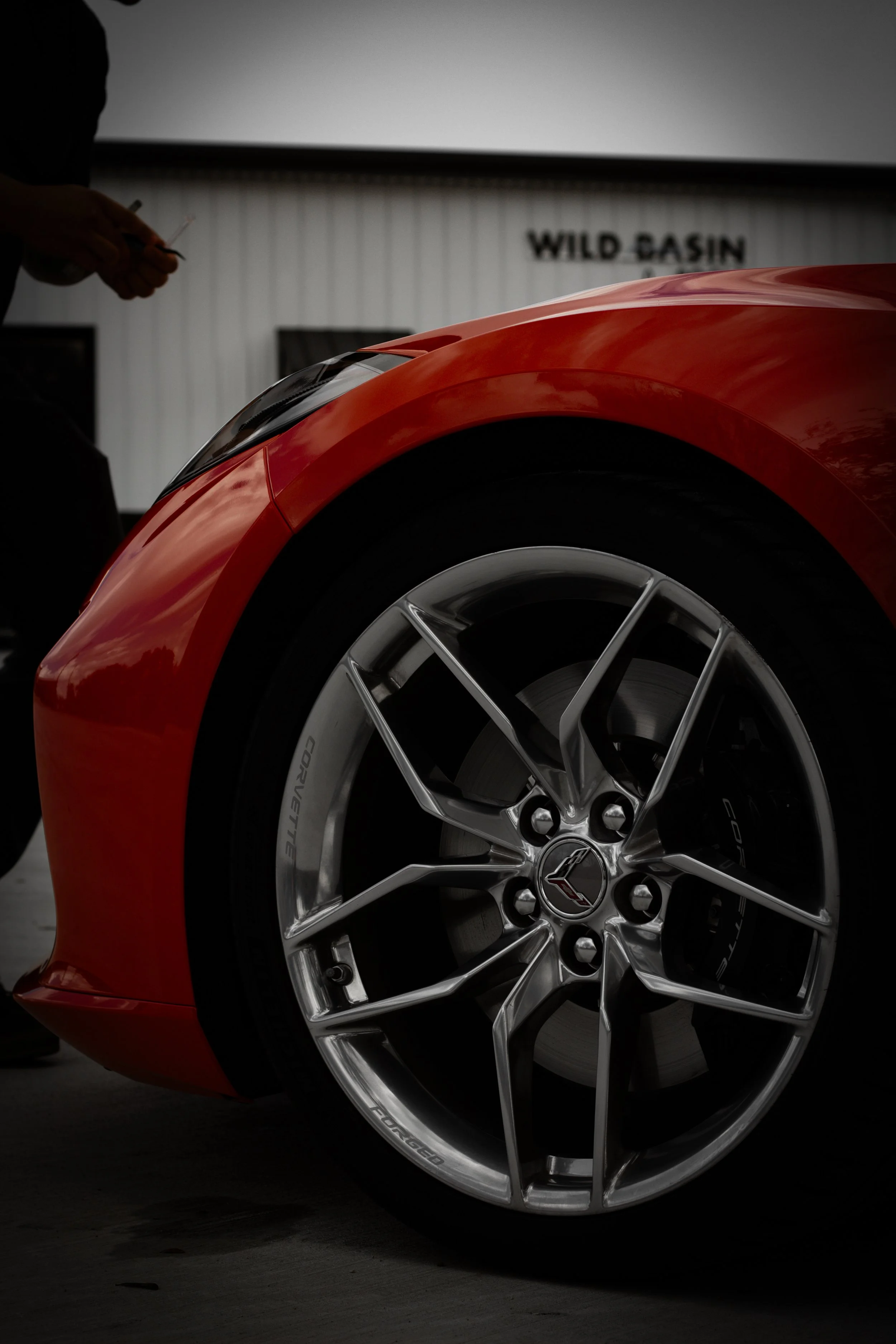Primer plano de la rueda de un automóvil deportivo rojo con el logo de Chevrolet en el centro, en un entorno con sombra y un fondo con un cartel que dice 'WILD CASIN'