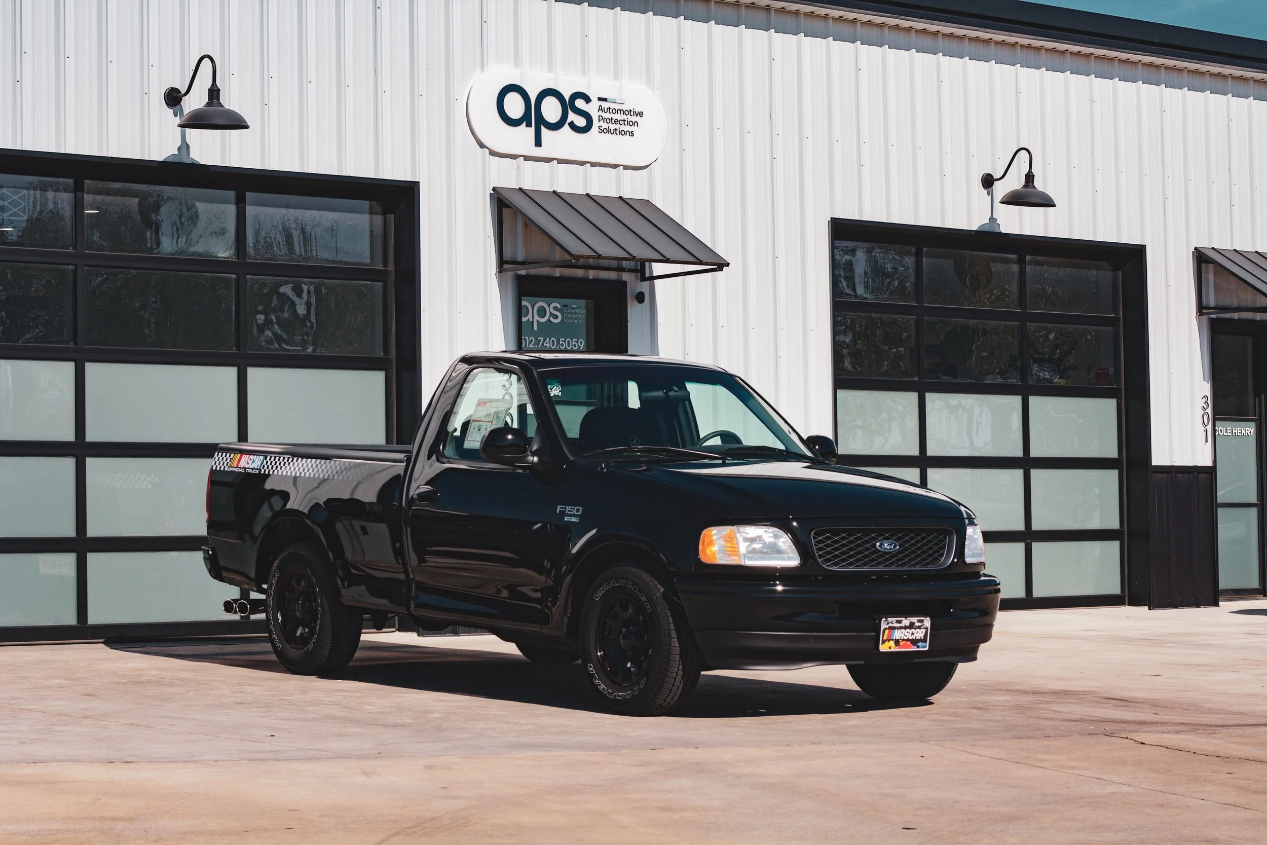 Camioneta negra Ford F150 estacionada frente a un edificio con señal de ASP y ventanas grandes.