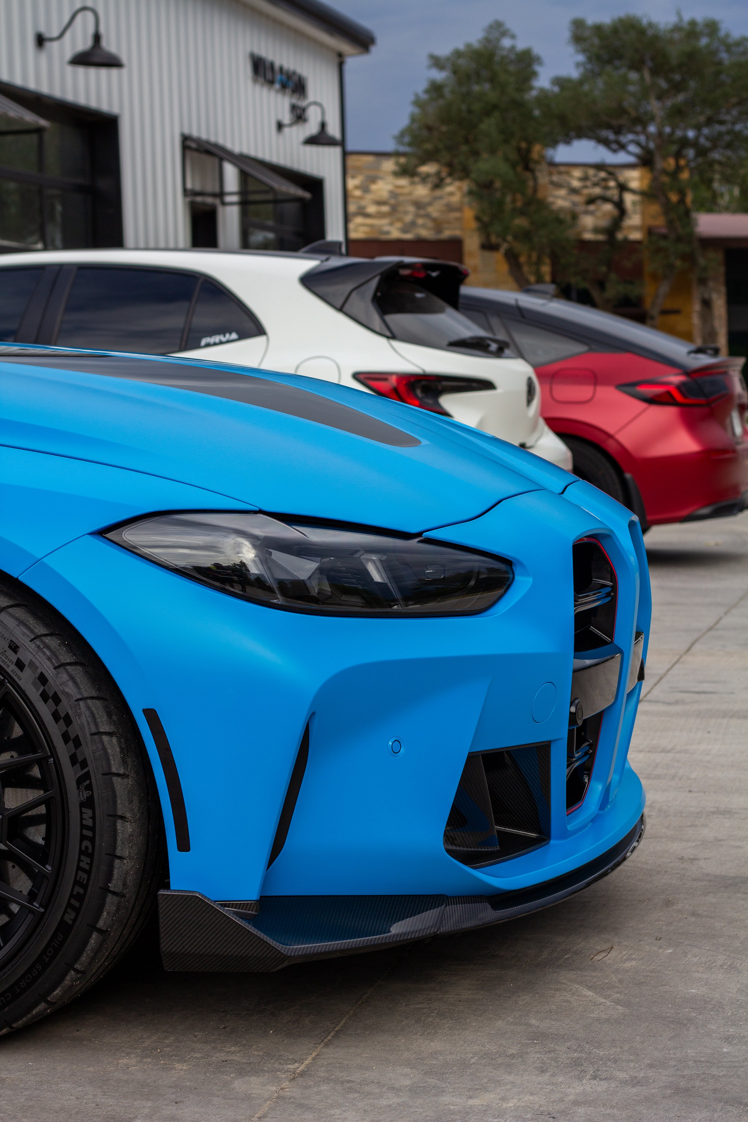 Tres autos deportivos de diferentes colores (azul, blanco y rojo) estacionados afuera de un edificio.