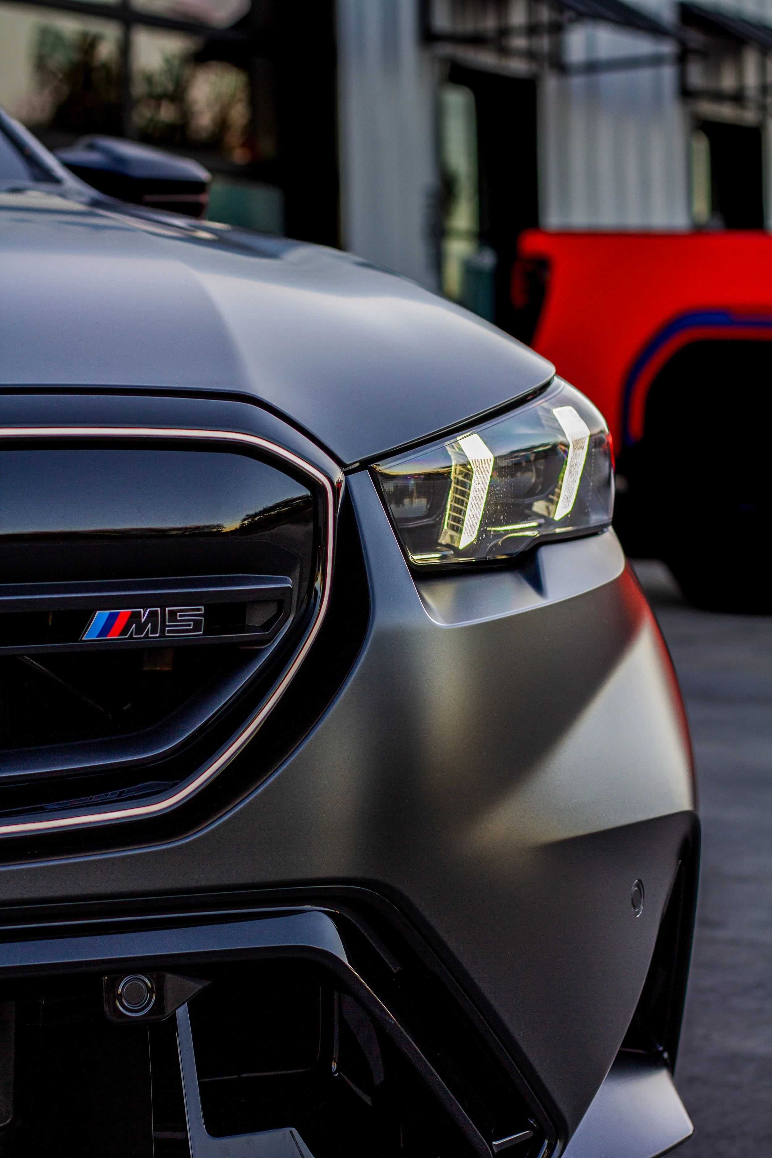Primer plano delantera de un auto deportivo negro, mostrando la parrilla, la insignia M5 y el diseño de las luces delanteras.