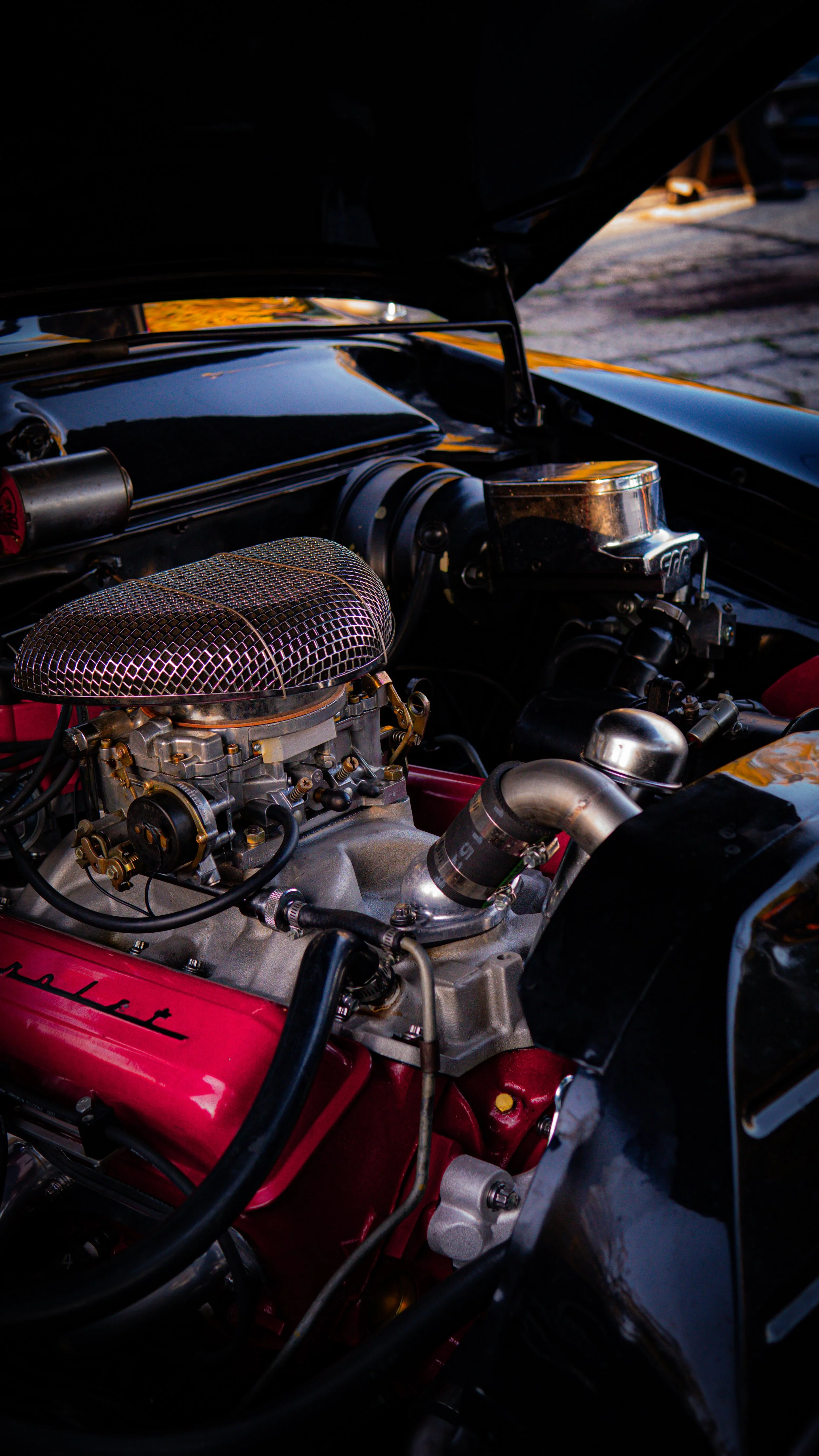 Motor de un automóvil clásico con componentes metálicos y filtro de aire de malla metálica, abierto el capó del vehículo.