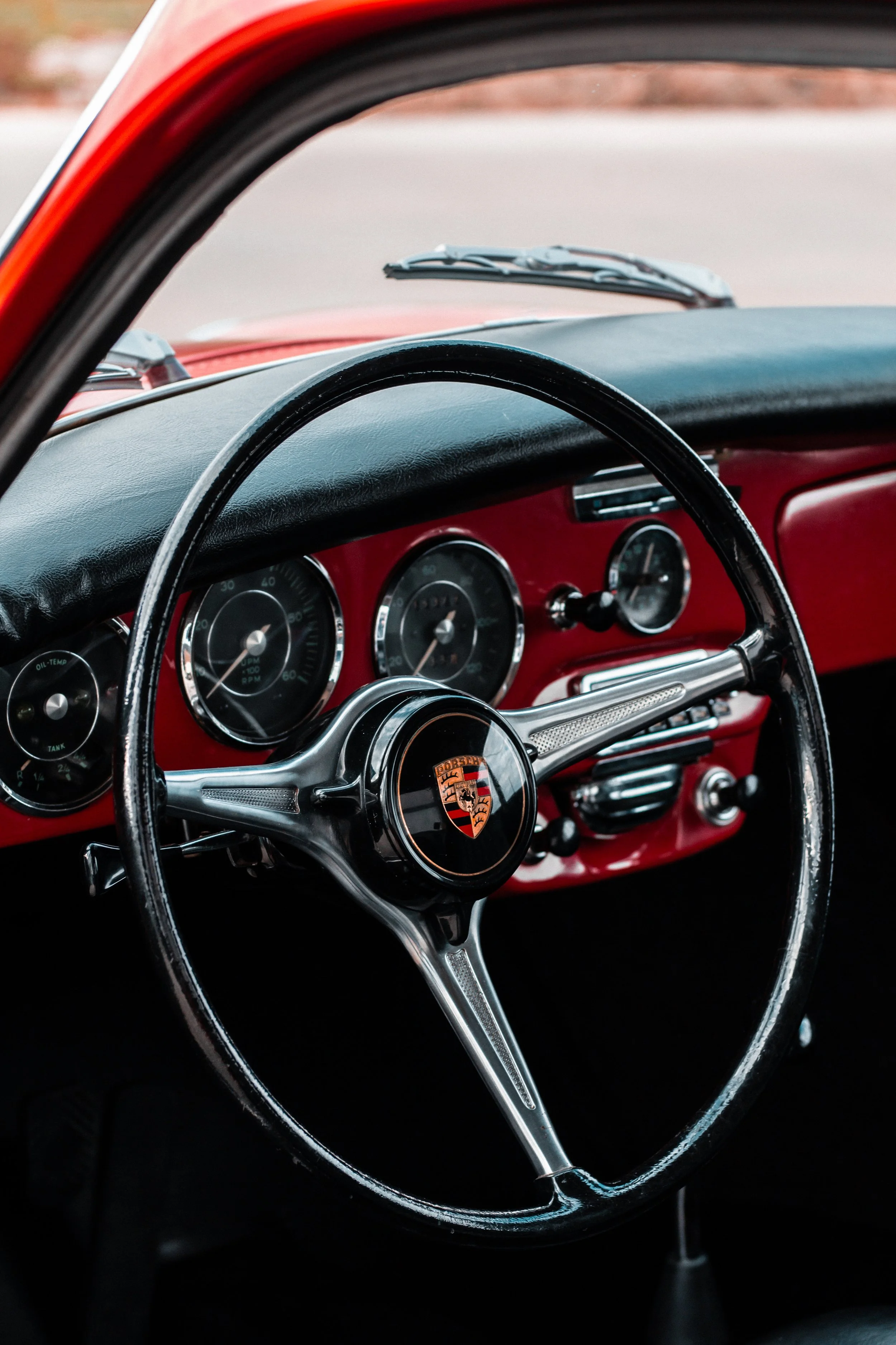 Interior de un coche clásico rojo con tablero y volante, el logo de Porsche en el centro del volante.