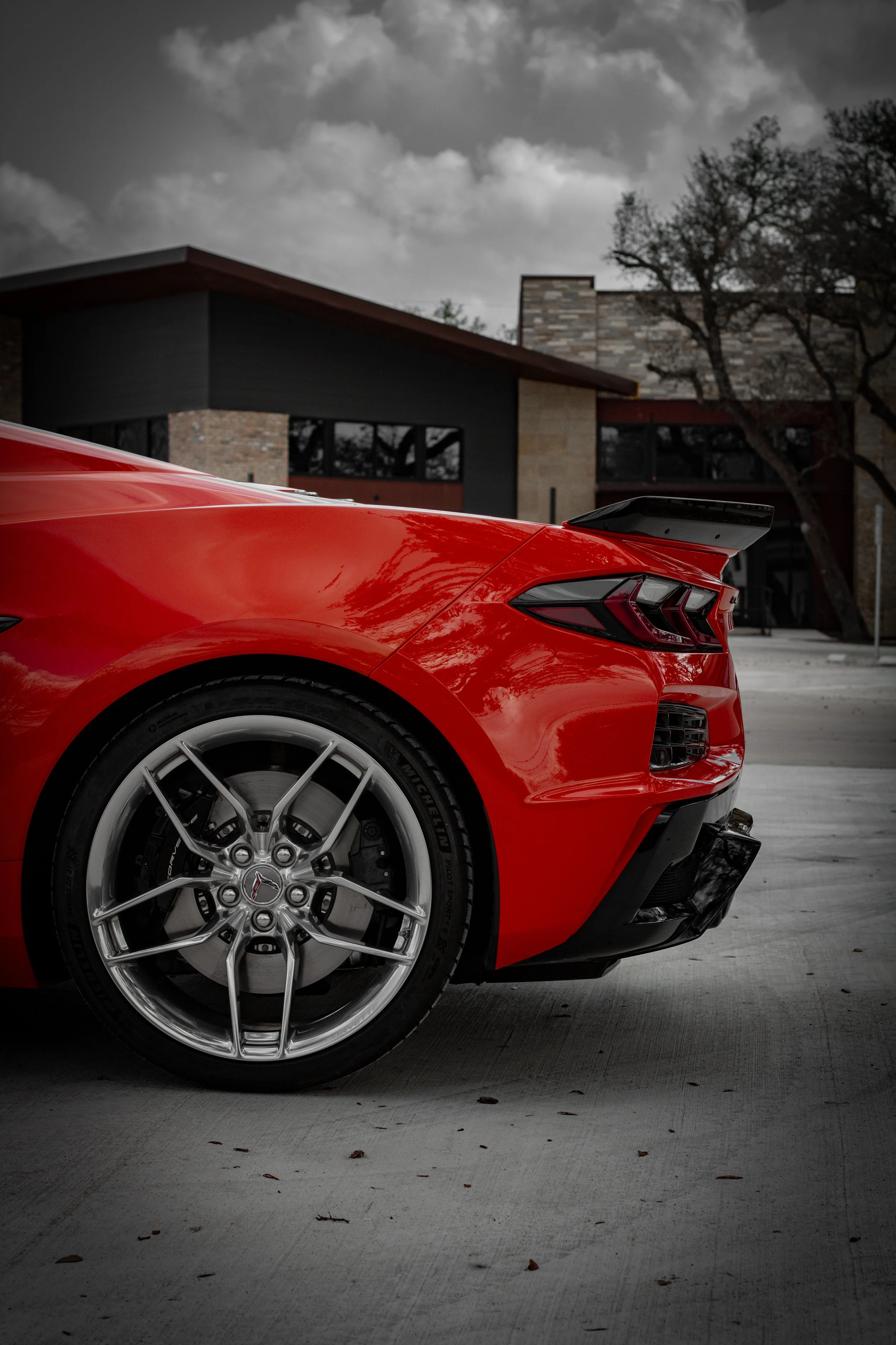 Autosportivo rojo en un estacionamiento con fondo de edificio moderno y cielo nublado.