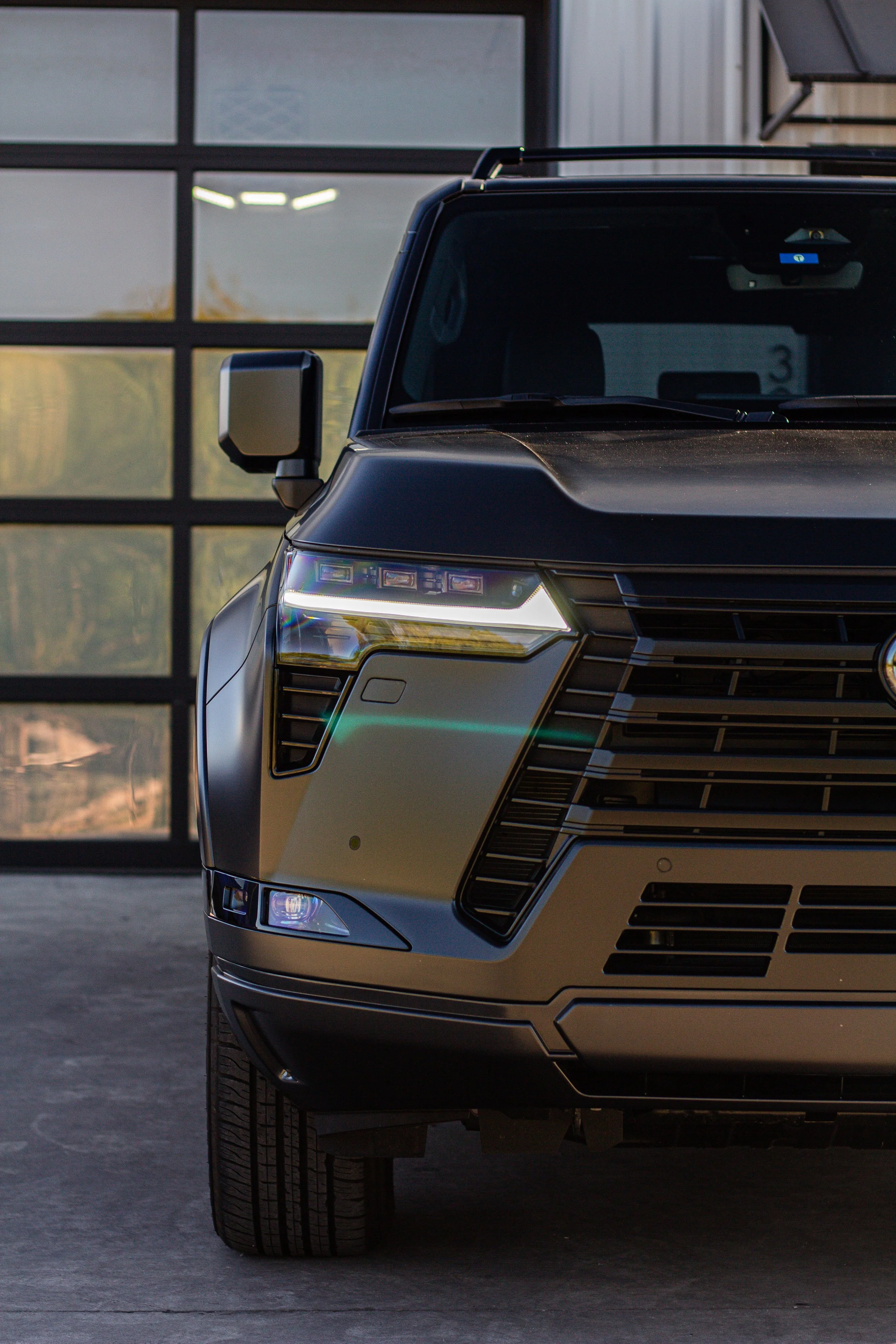 Frontal de un vehículo deportivo de color gris con faros LED, en un entorno de garaje o estacionamiento.