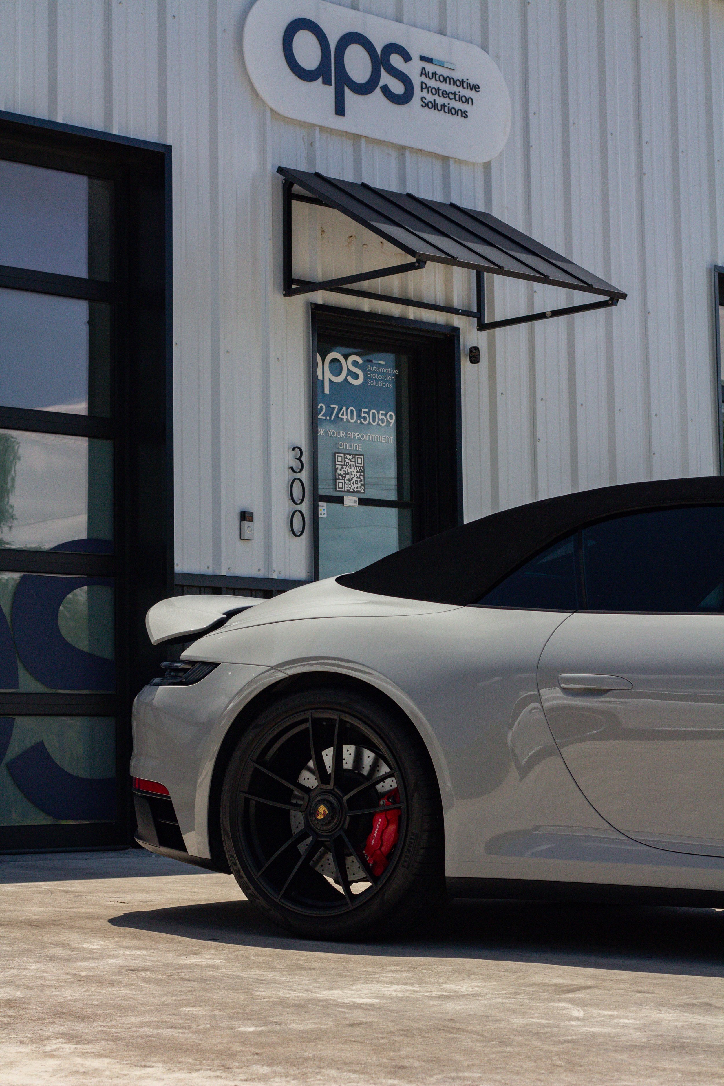 Edificio de protección automotriz con un automóvil deportivo gris y logotipoAPS en la fachada.