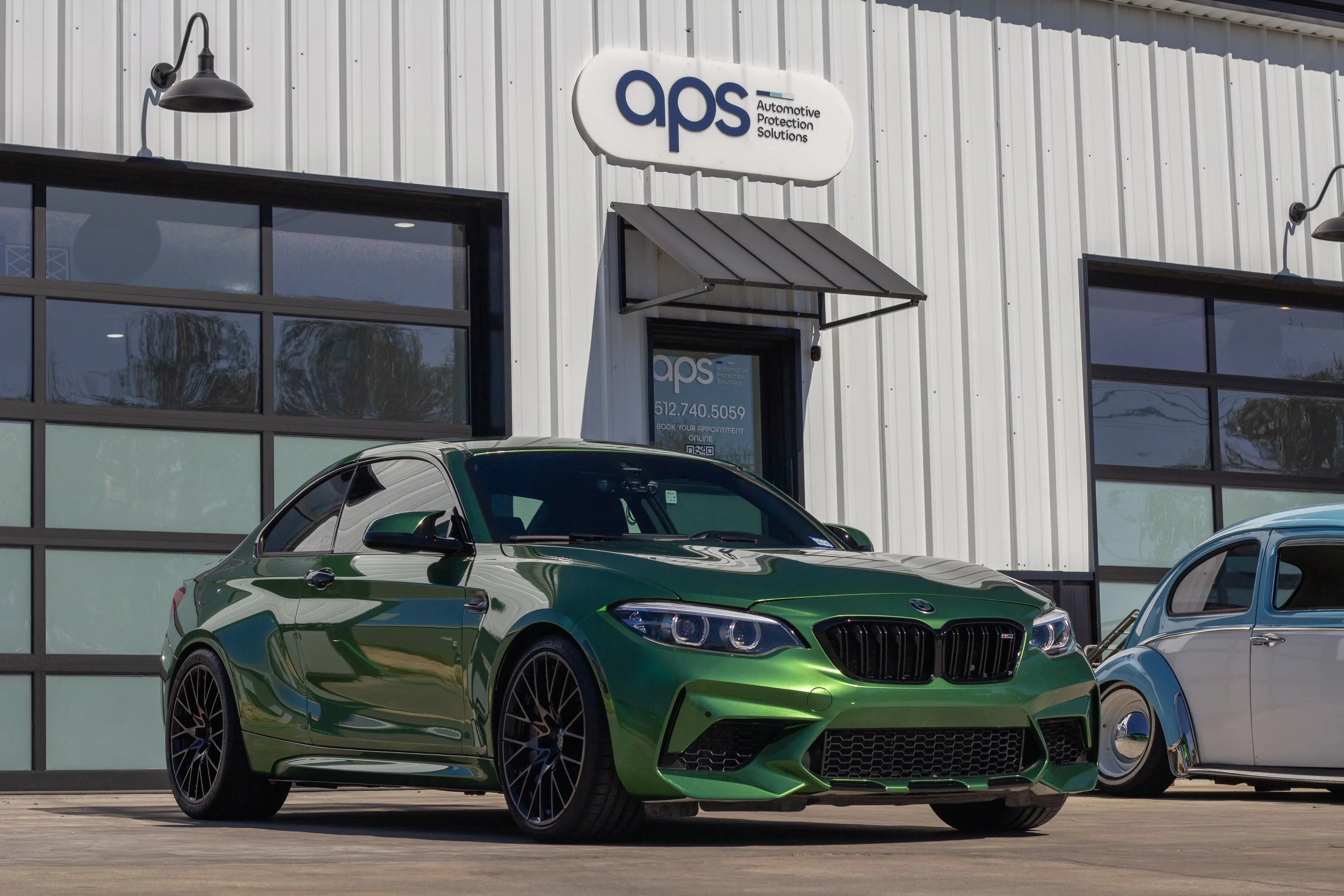 Auto verde deportivo frente a un taller de reparación, con cartel de APS en la fachada.