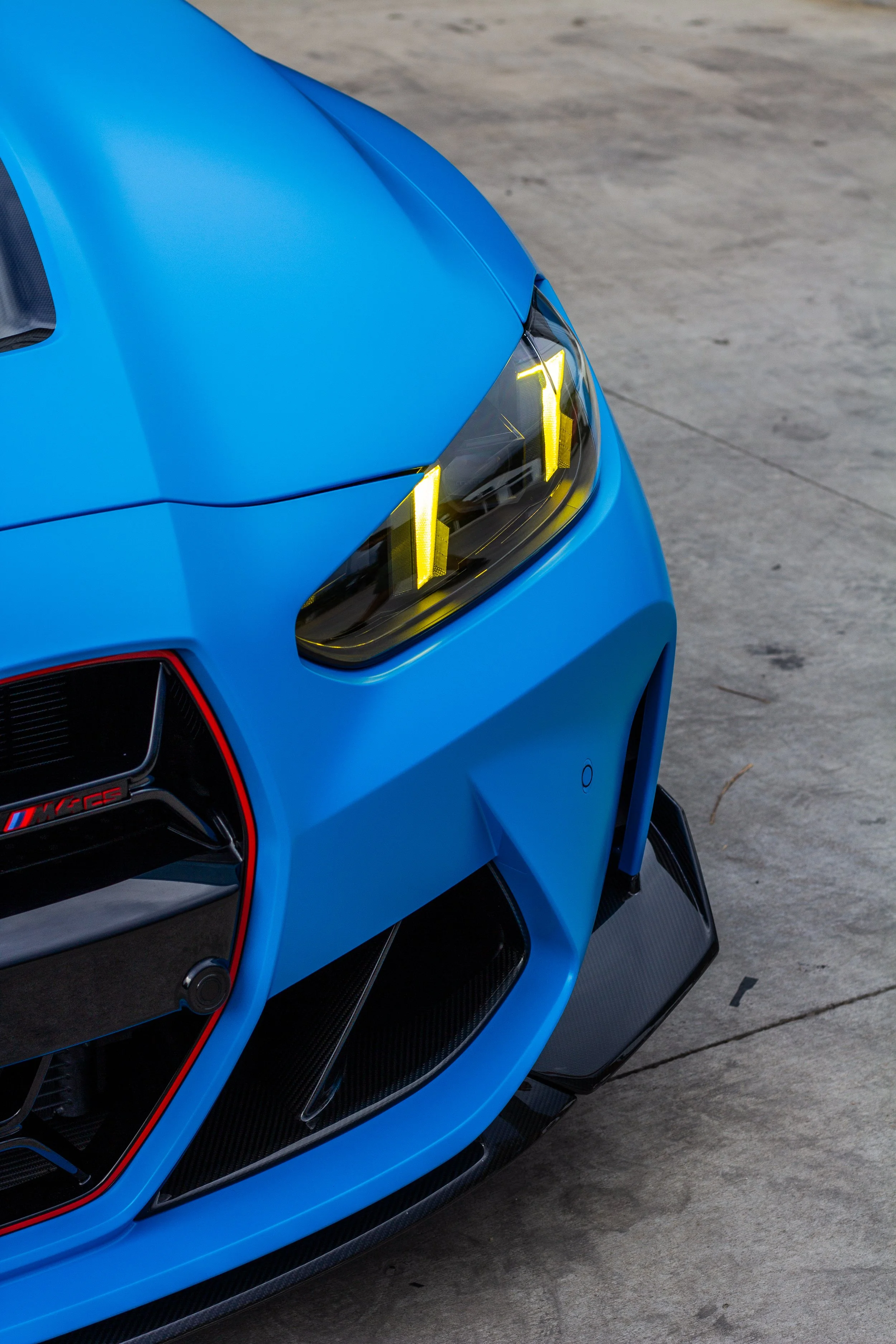 Parte frontal de un coche deportivo azul con detalles en negro y faros delanteros de luz amarilla.