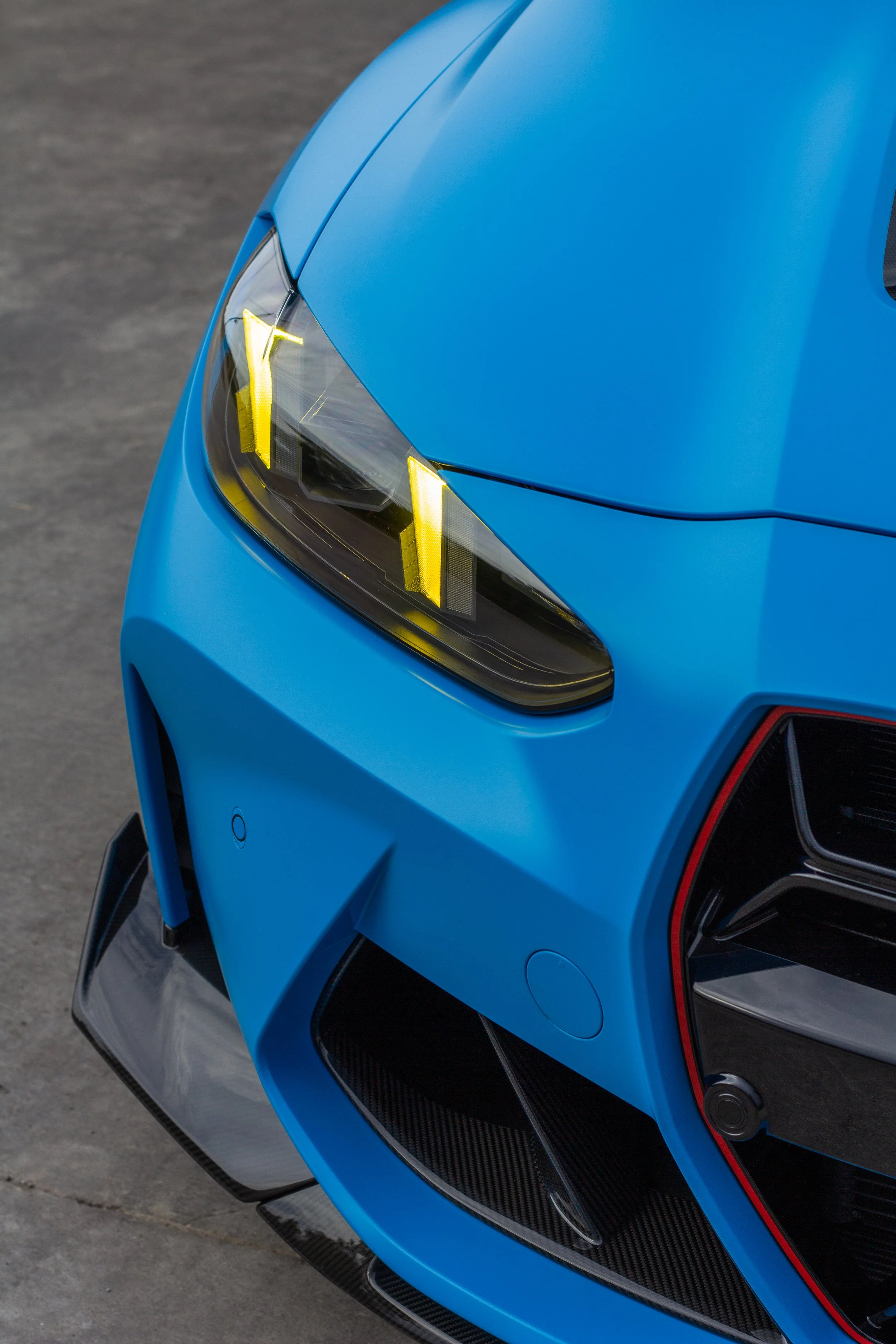 Primer plano de la parte delantera de un auto deportivo azul, mostrando la cabeza delantera y la luz delantera con detalles en amarillo y el diseño aerodinámico.