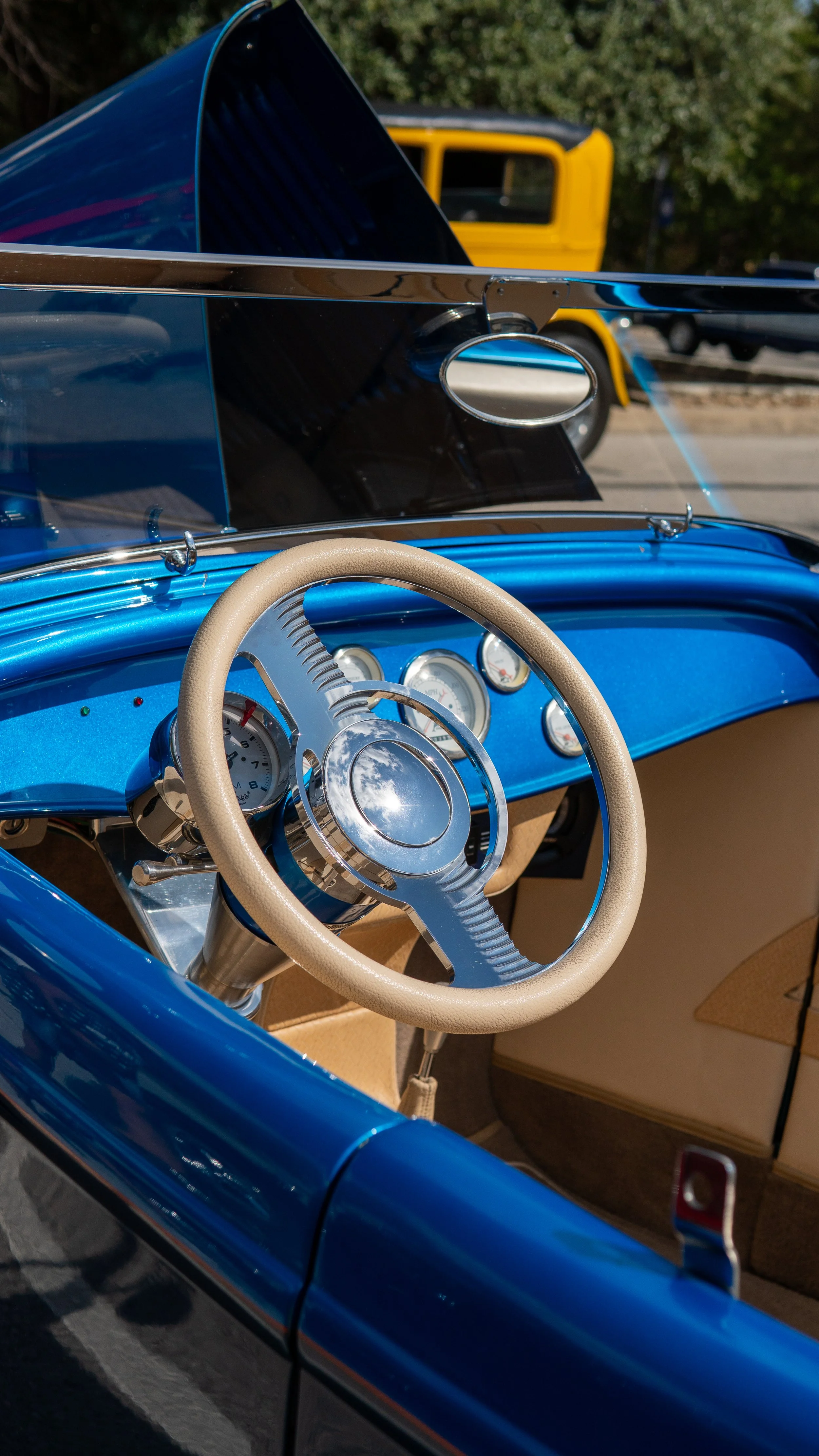 Interiores de un coche clásico de color azul con volante beige, tablero con instrumentos y capota de cristal.
