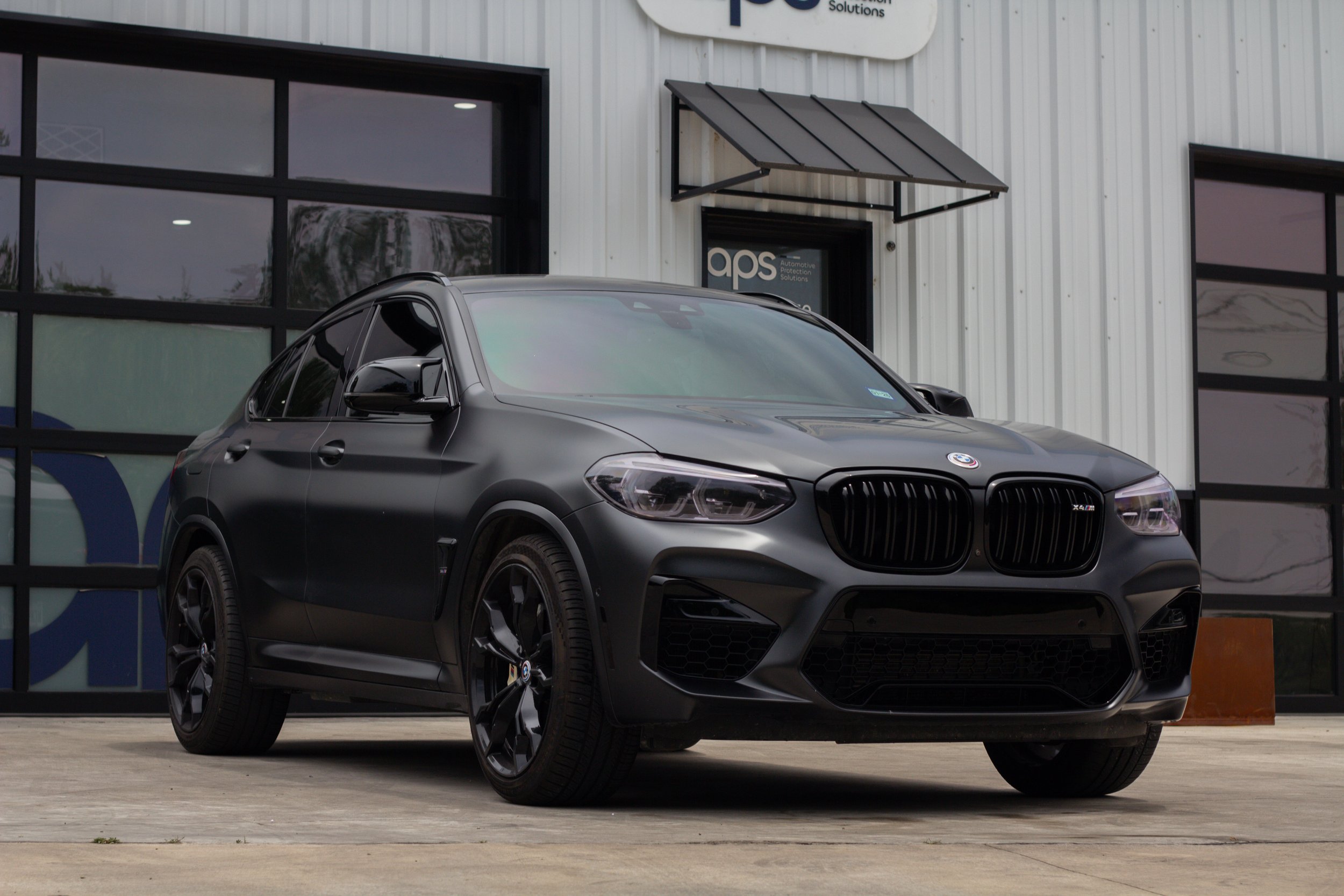 Auto negro BMW X4 estacionado frente a un edificio con paredes de metal y ventanas grandes.