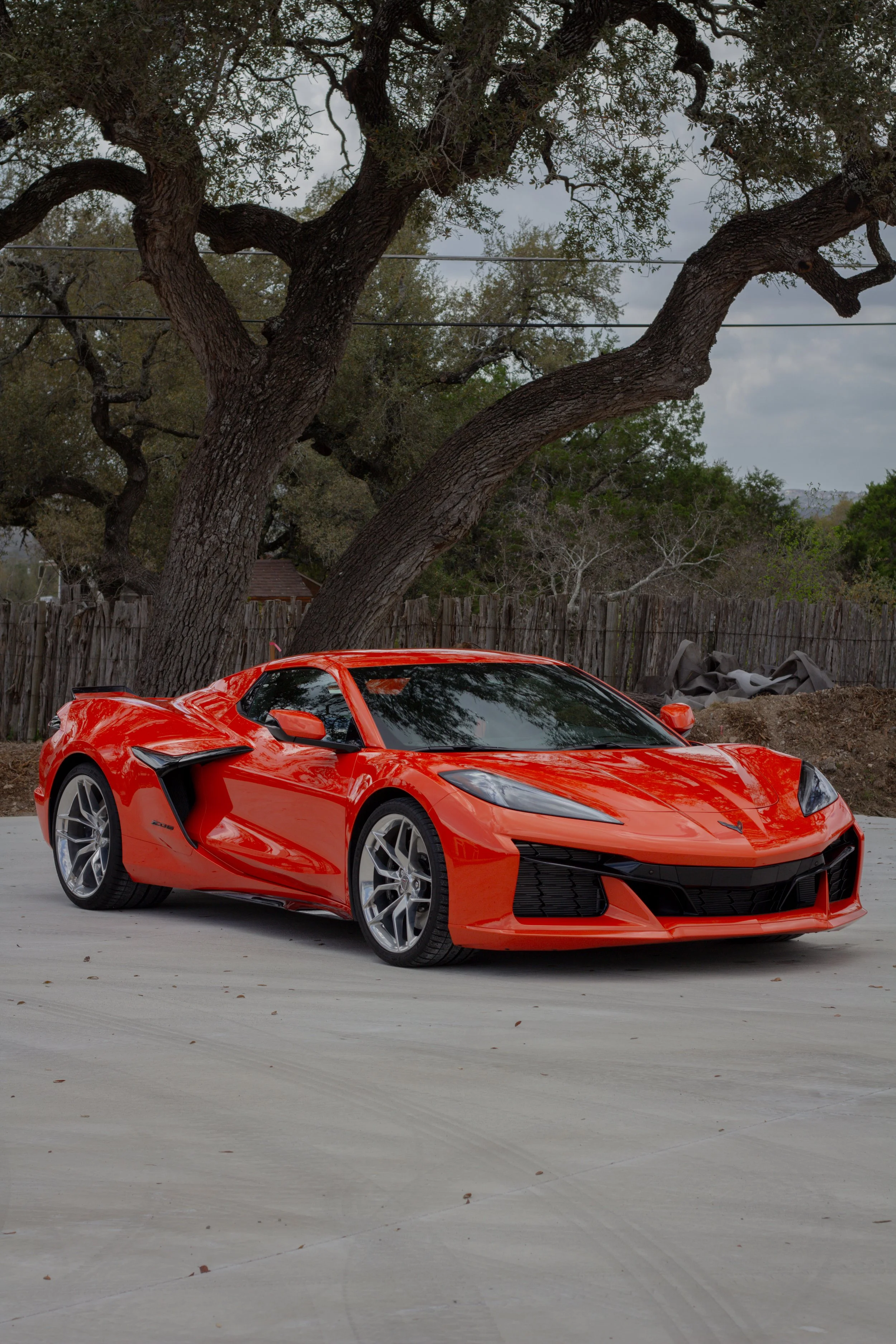 Coche deportivo rojo en un espacio abierto con árboles y cielo nublado