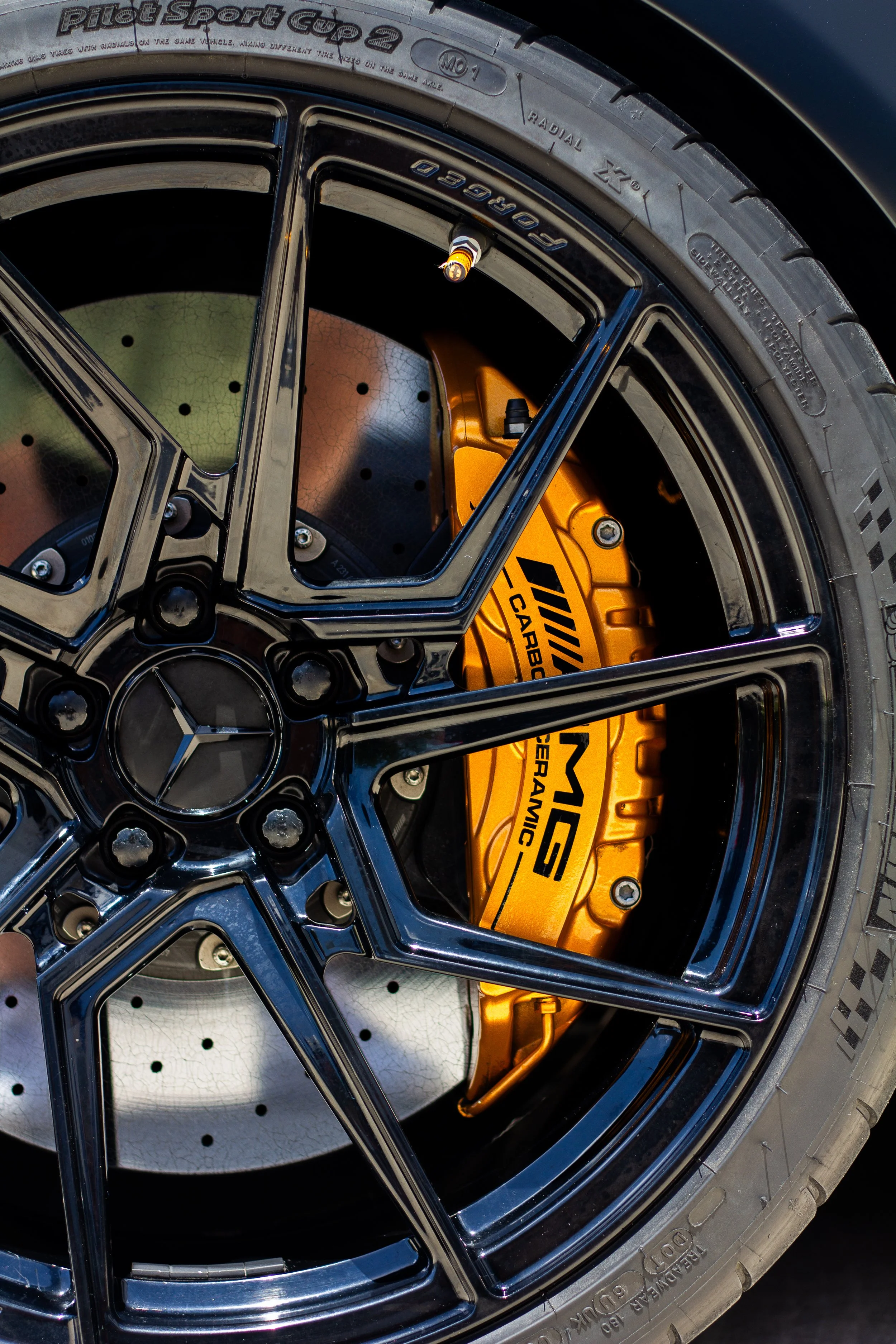 Vista de un neumático de alto rendimiento con un freno de disco de alta tecnología y una pinza de freno dorada con la marca AMG, en un coche Mercedes-Benz de alto rendimiento.
