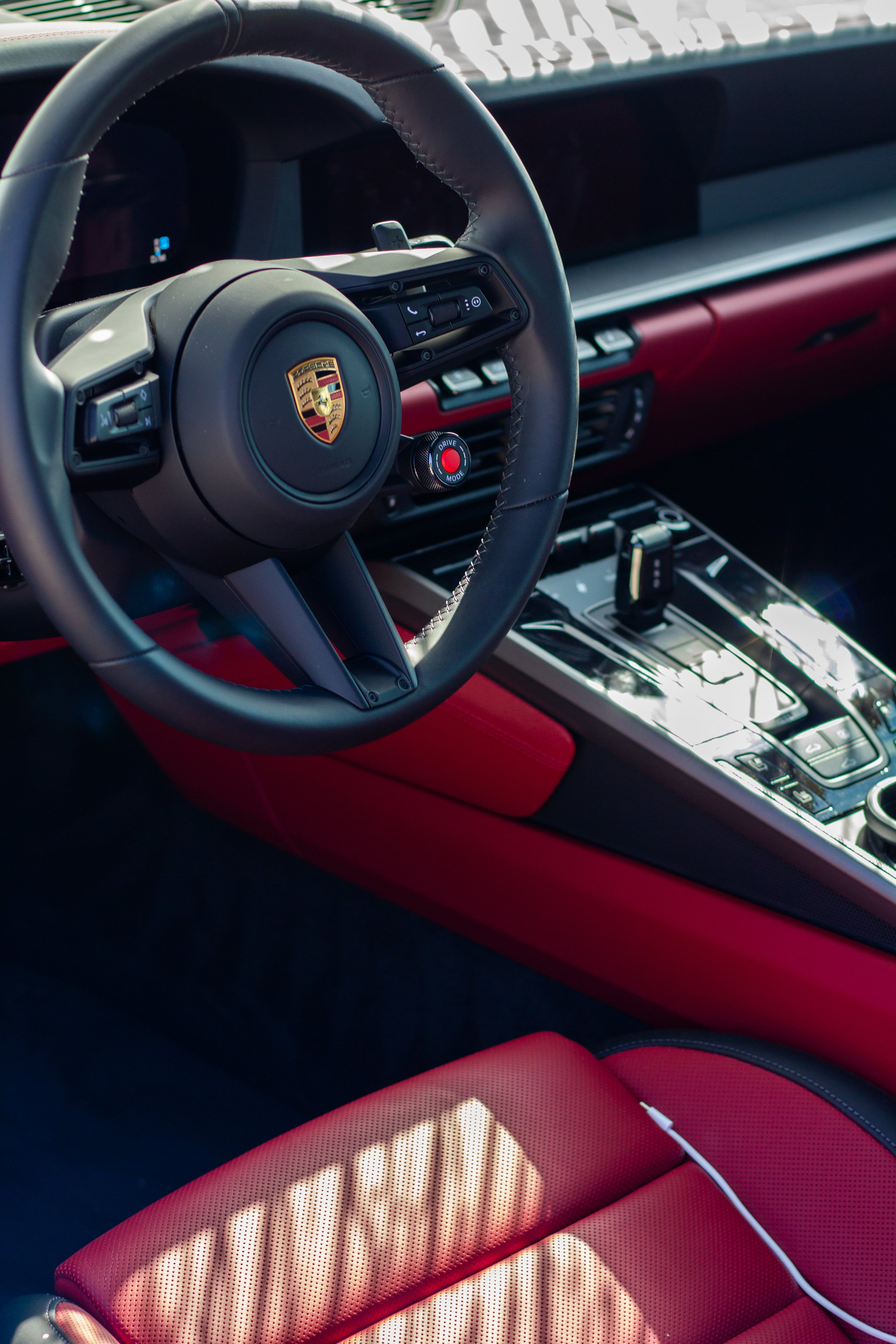Interior de un coche Porsche con volante, consola central y asiento en tonos rojos.