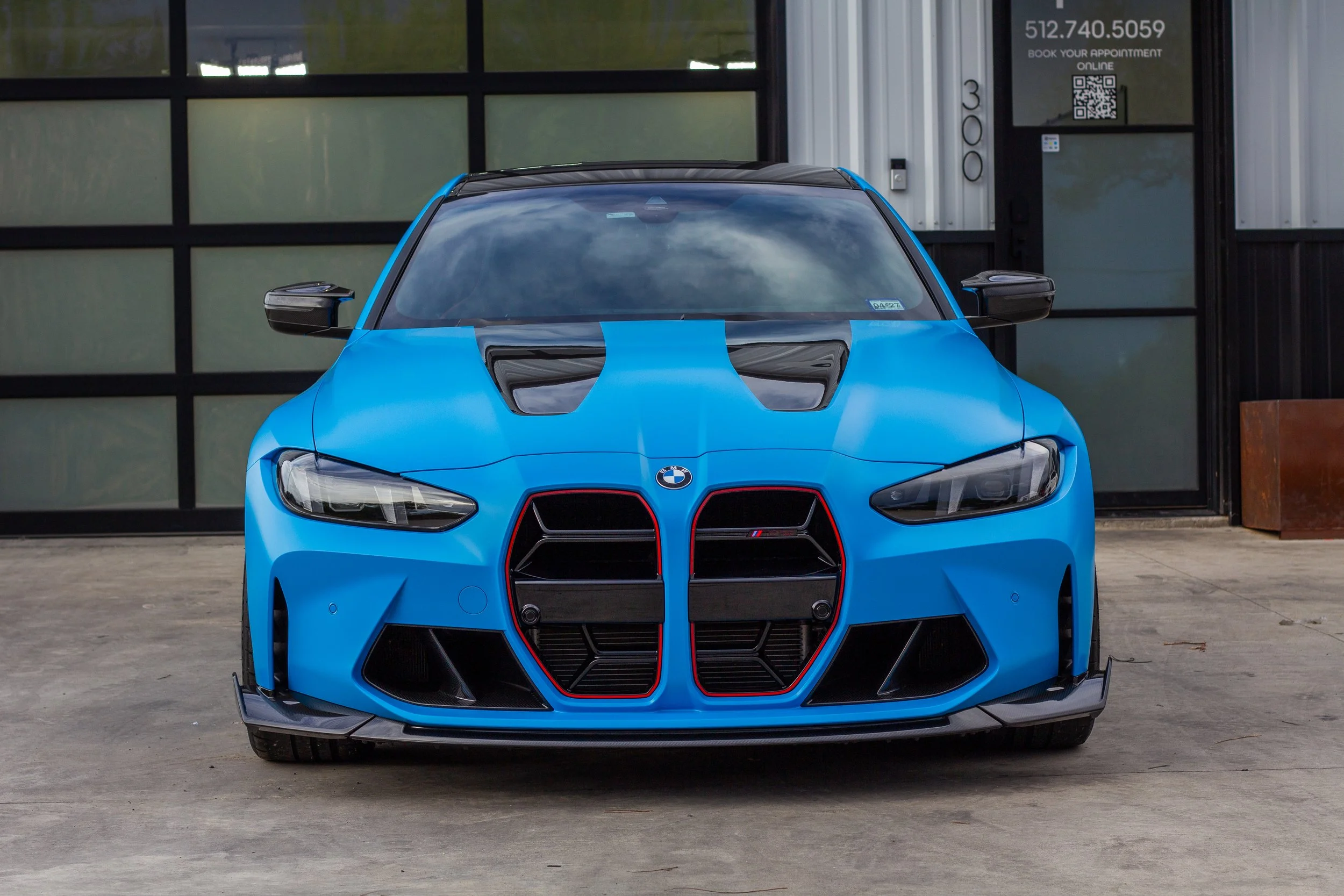 Coche deportivo BMW M2 en color azul con detalles en negro, frente a un edificio de estilo industrial.