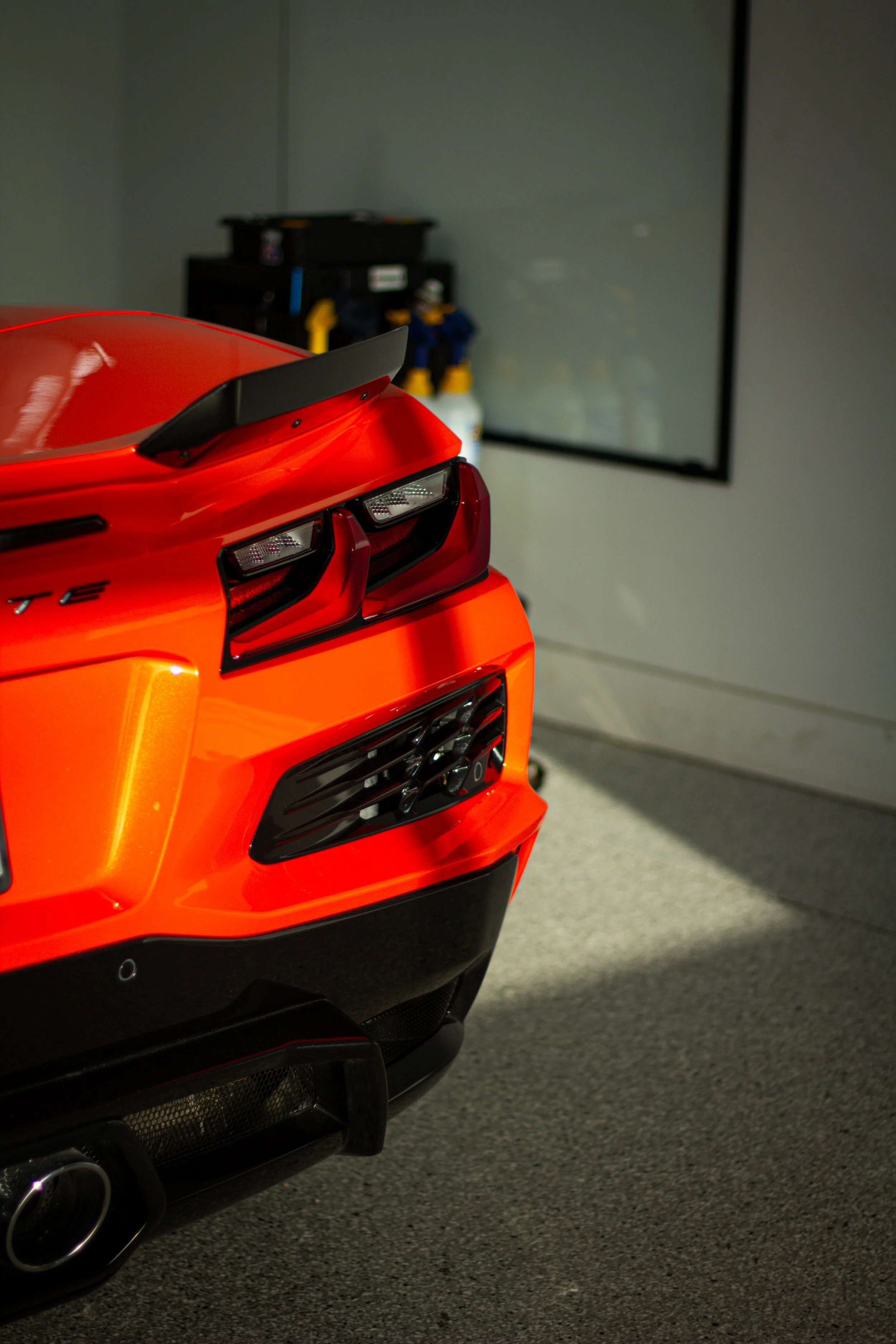 Parte trasera de un coche deportivo naranja en un garaje, con detalles de luz y sombra.