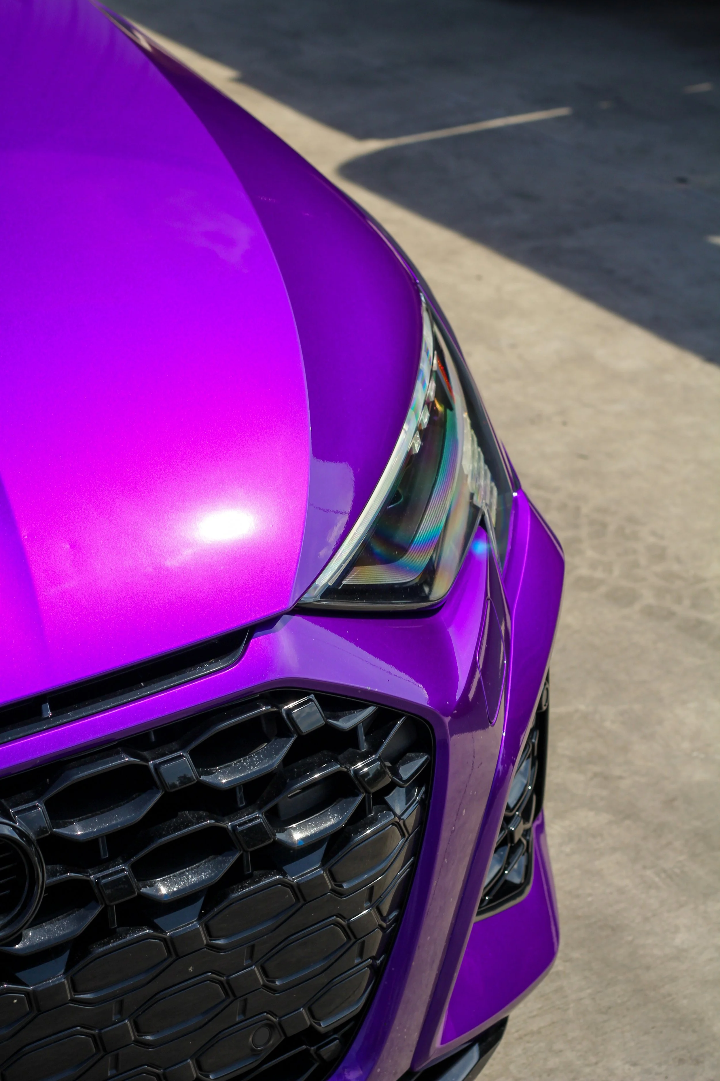 Primer plano de la parte delantera de un auto de color púrpura, mostrando la parrilla y la luz delantera.