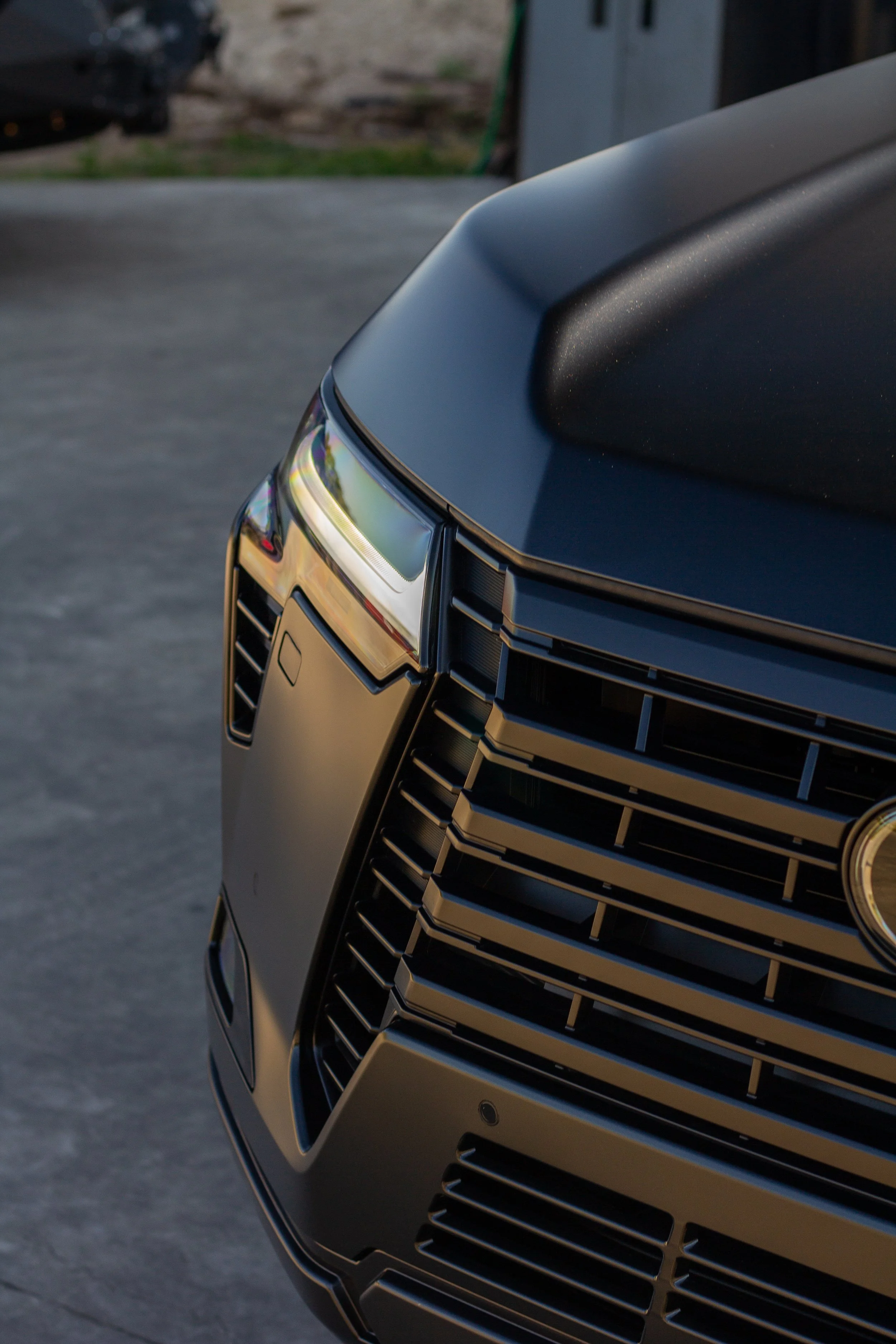 Primer plano del frontis de un automóvil negro, mostrando la parrilla y la cabeza de la luz delantera.