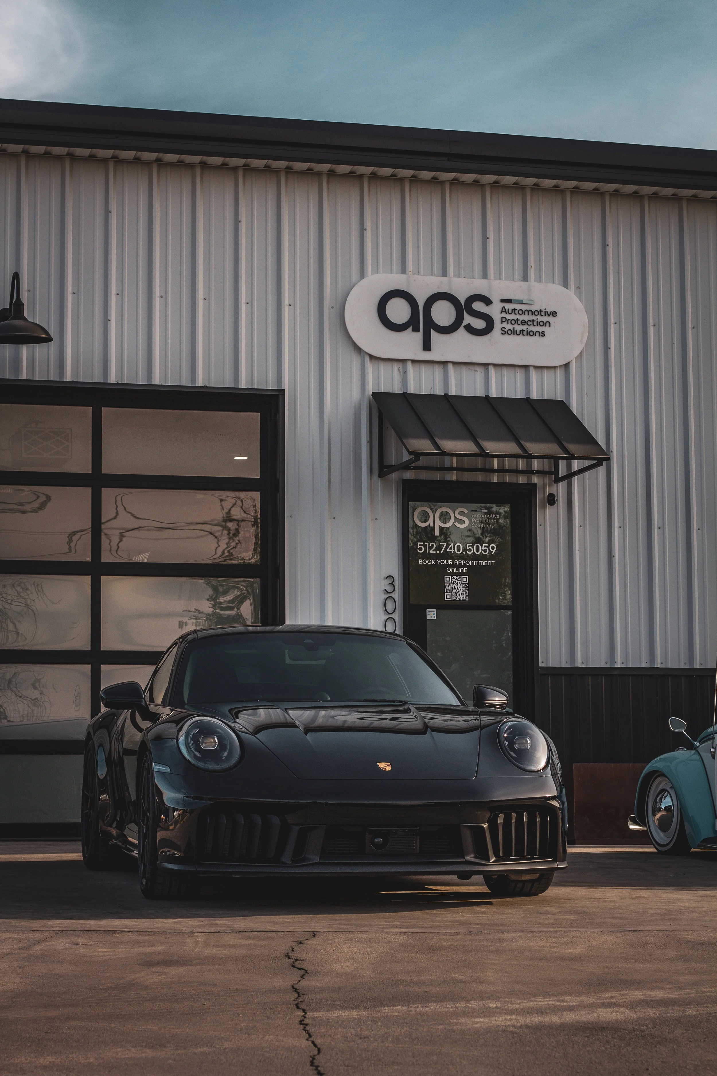 Edificio con un cartel que dice 'aps', con un coche deportivo negro estacionado frente a la entrada.
