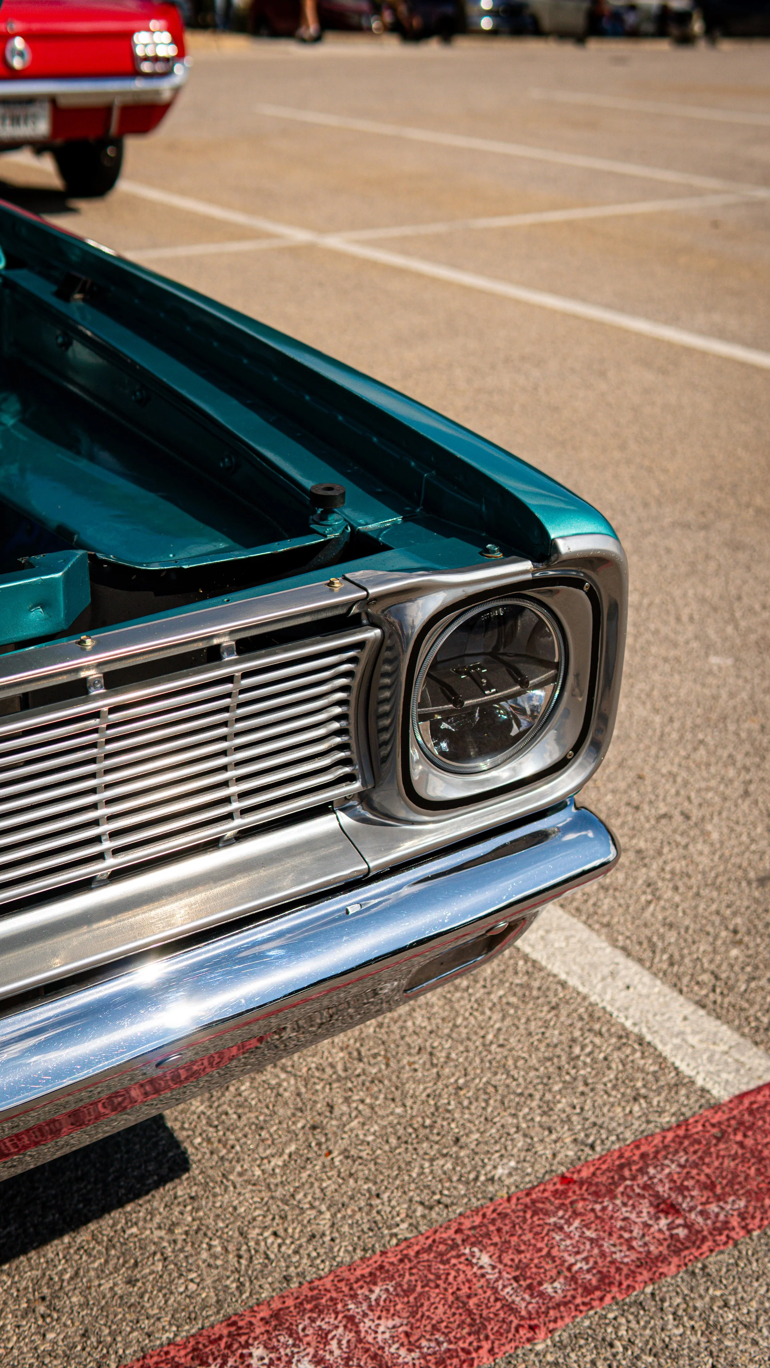 Primer plano del extremo frontal de un coche clásico, mostrando la parrilla, la cabeza de la luz y parte del capó en un estacionamiento.