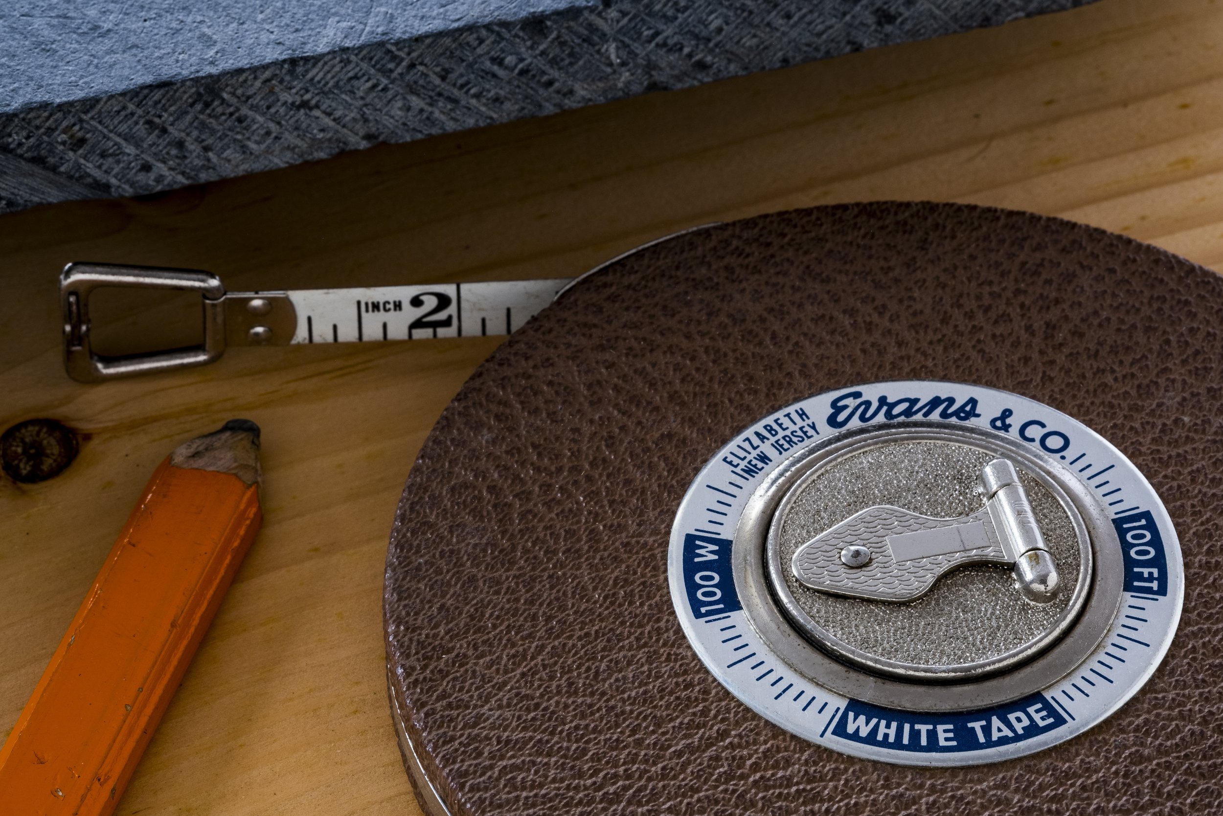 Close-up of a tape measure, a sanding pad, an orange utility knife, and part of a wooden surface.