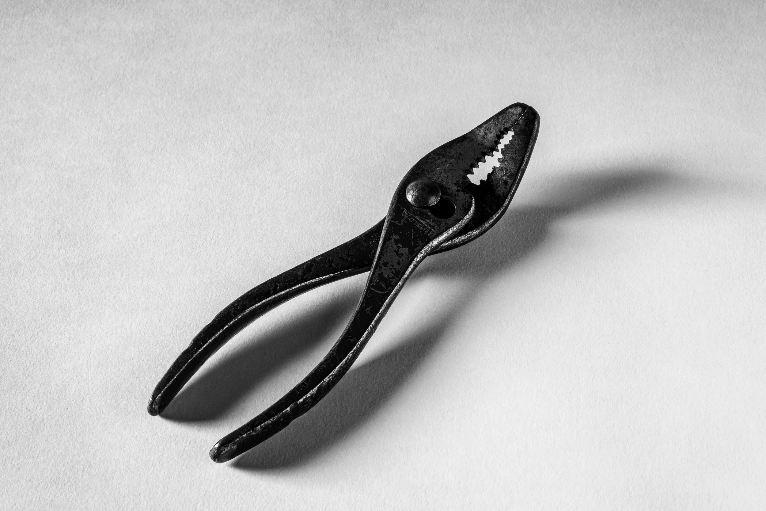 A close-up of a vintage metal can opener on a white surface.
