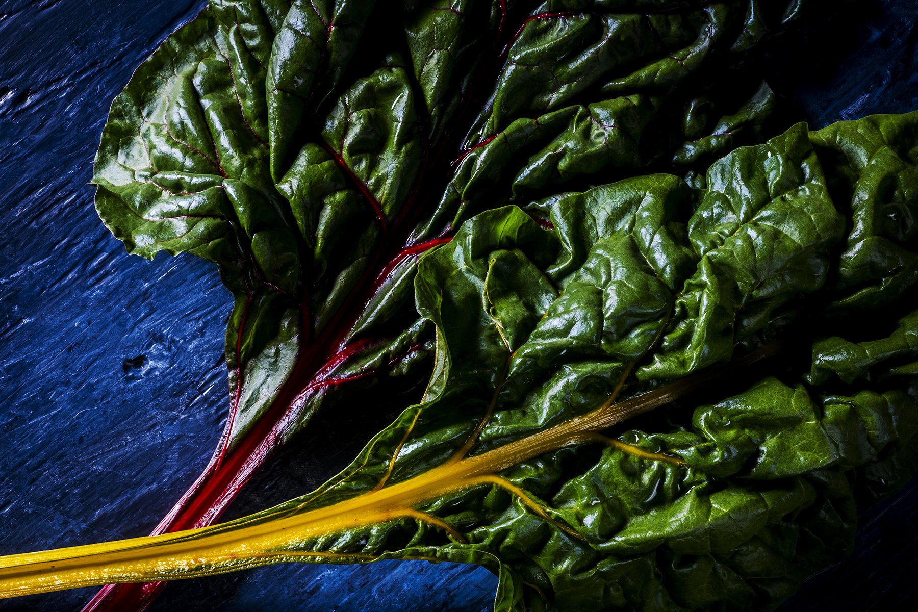 Fresh Swiss chard leaves with red stems and yellow stems on a dark wooden surface.