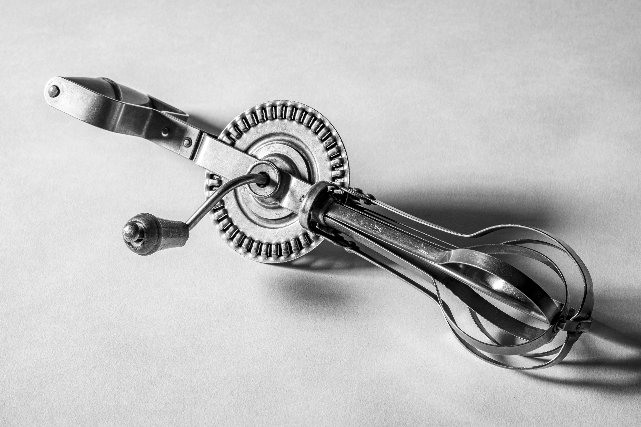 Black and white photo of a manual can opener on a flat surface.