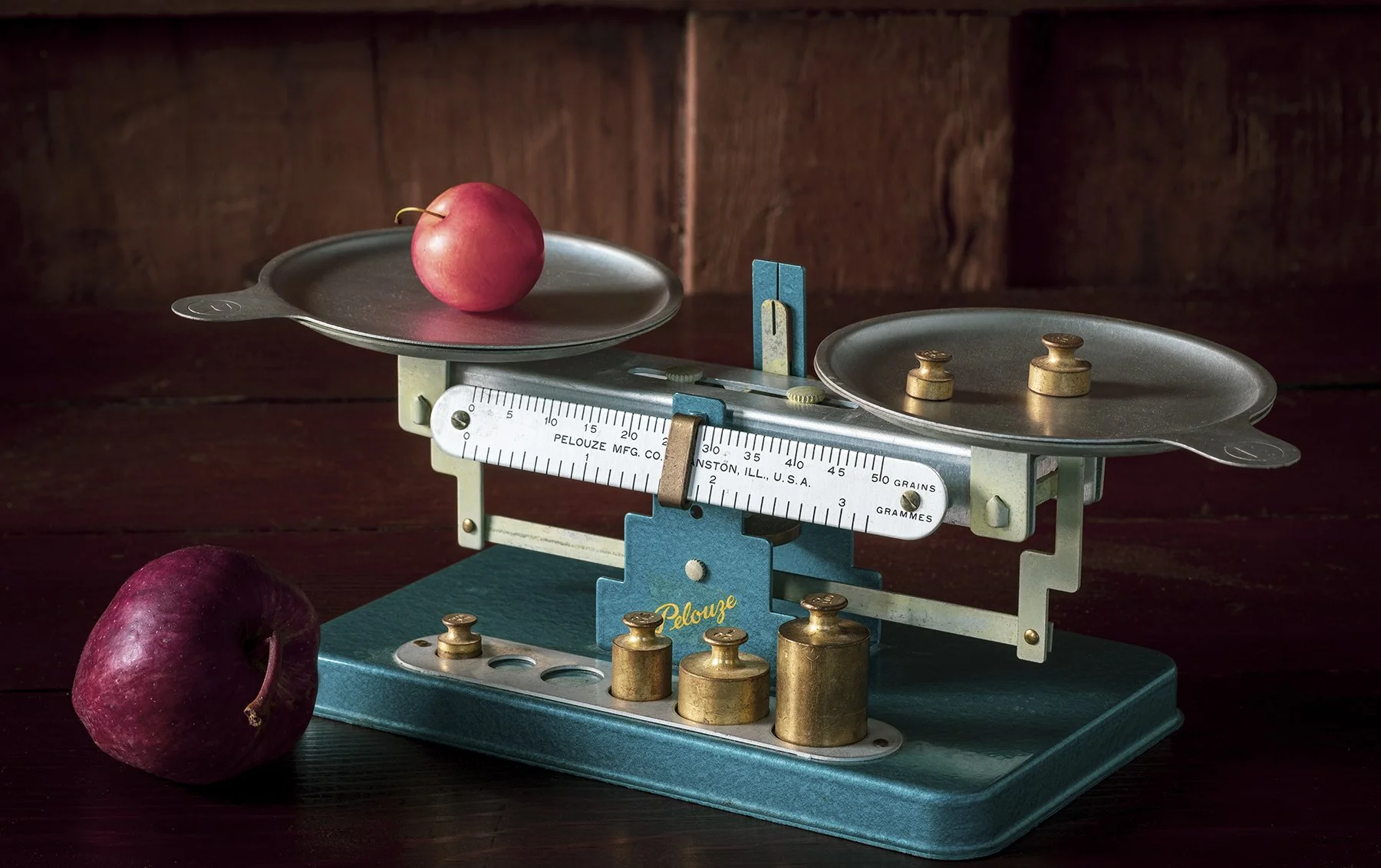 Vintage kitchen scale with red apples, a wooden background, and a cherry in the foreground.