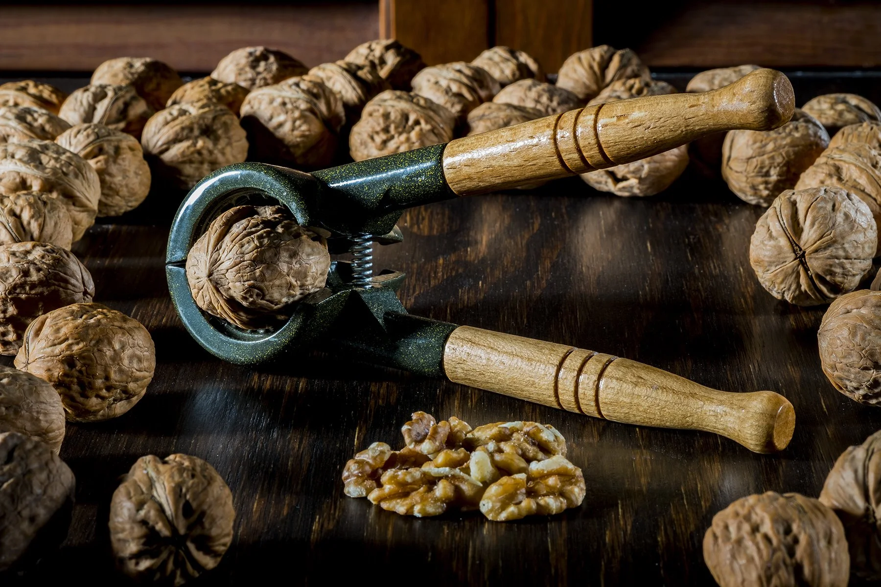 Walnut cracking tools surrounded by walnuts on a dark wooden surface.