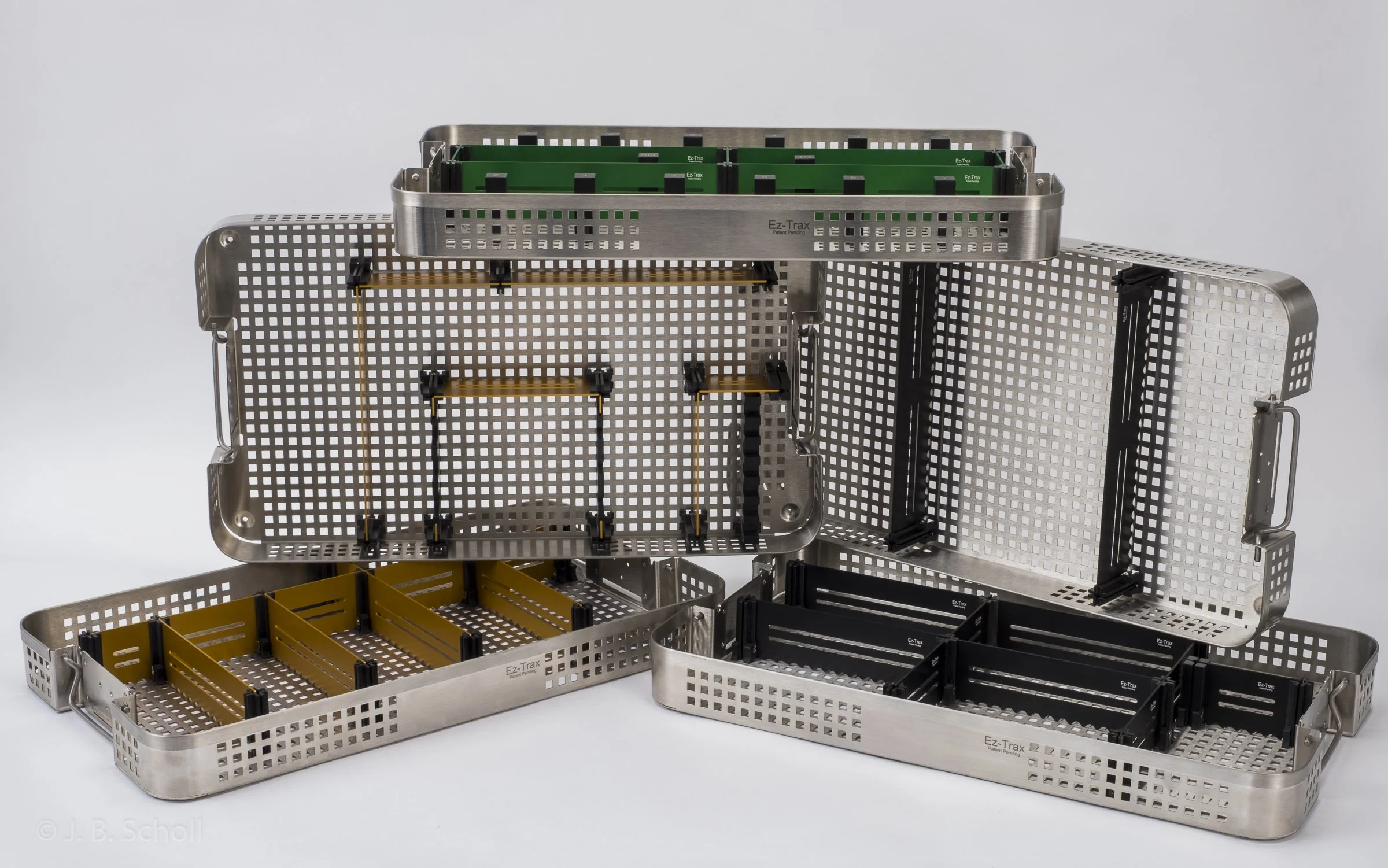 Multiple stainless steel medical storage trays and containers, some with black and yellow dividers, arranged on a white background.