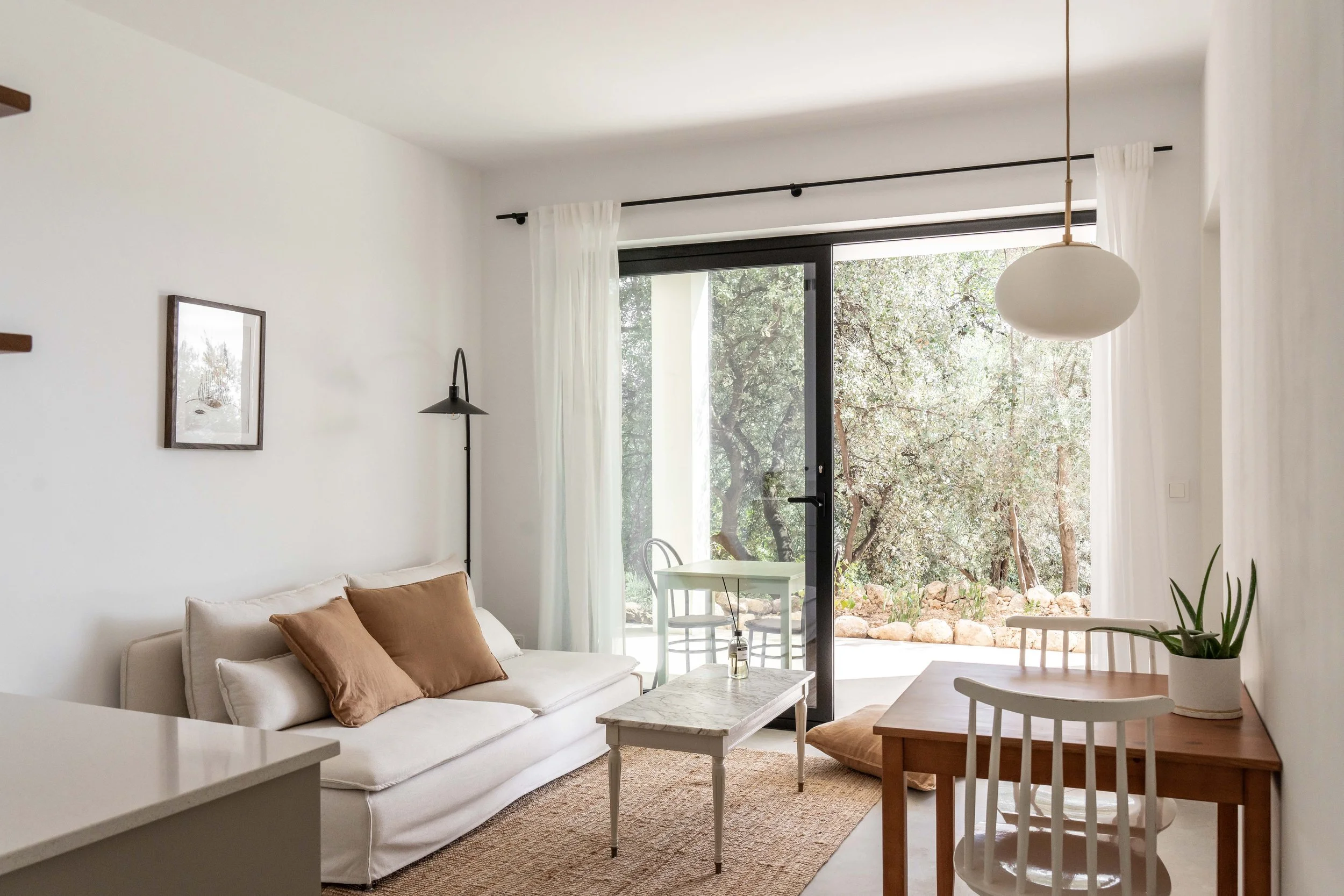 Woonkamer met zithoek, eettafel, planten, grote schuifdeur die naar de veranda leidt.