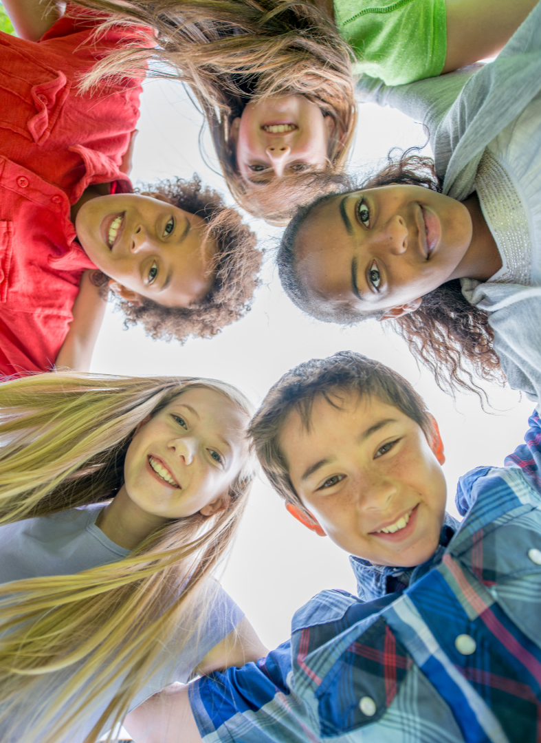 Group of children looking down at the camera, smiling and sticking their tongues out outdoors against the sky.
