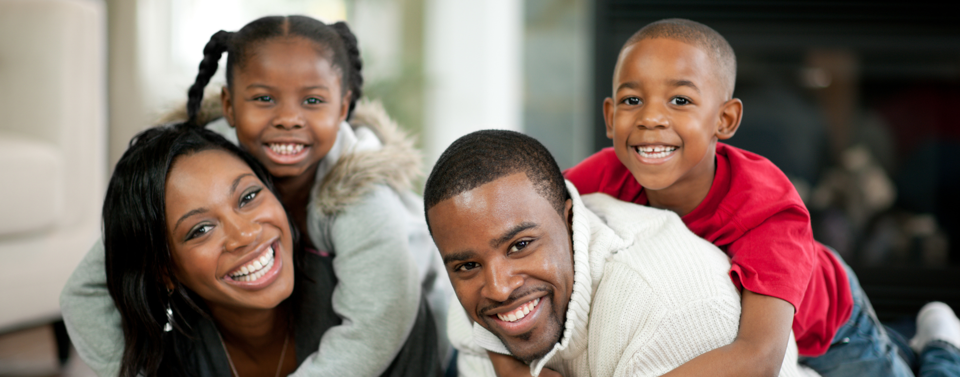 A smiling family of four, including a mother, father, daughter, and son, posing together indoors.