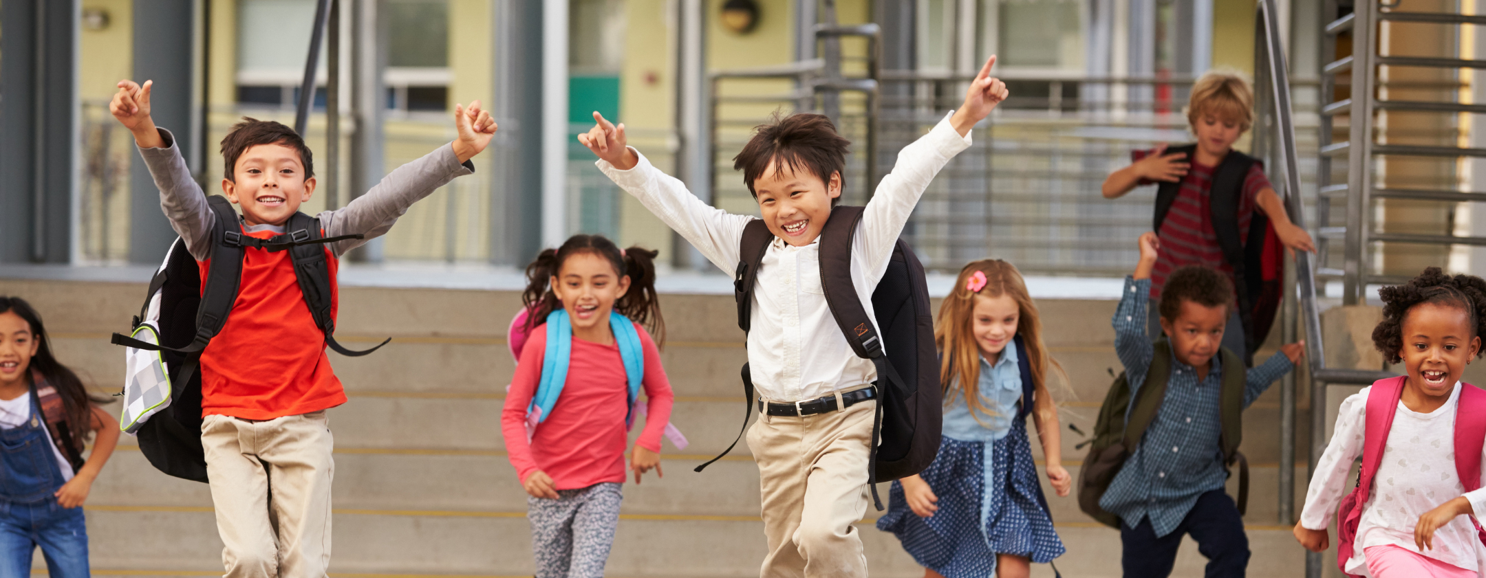 Happy children with backpacks leaving school, running down stairs and waving.