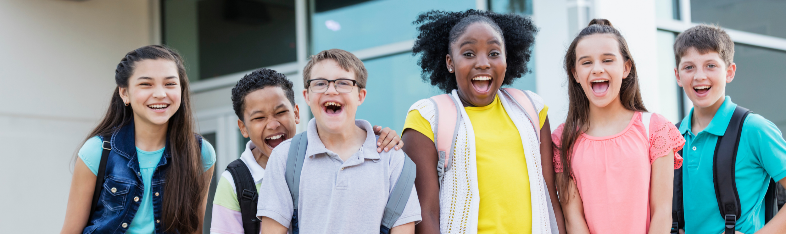 Group of six diverse school children smiling and laughing outside a building.